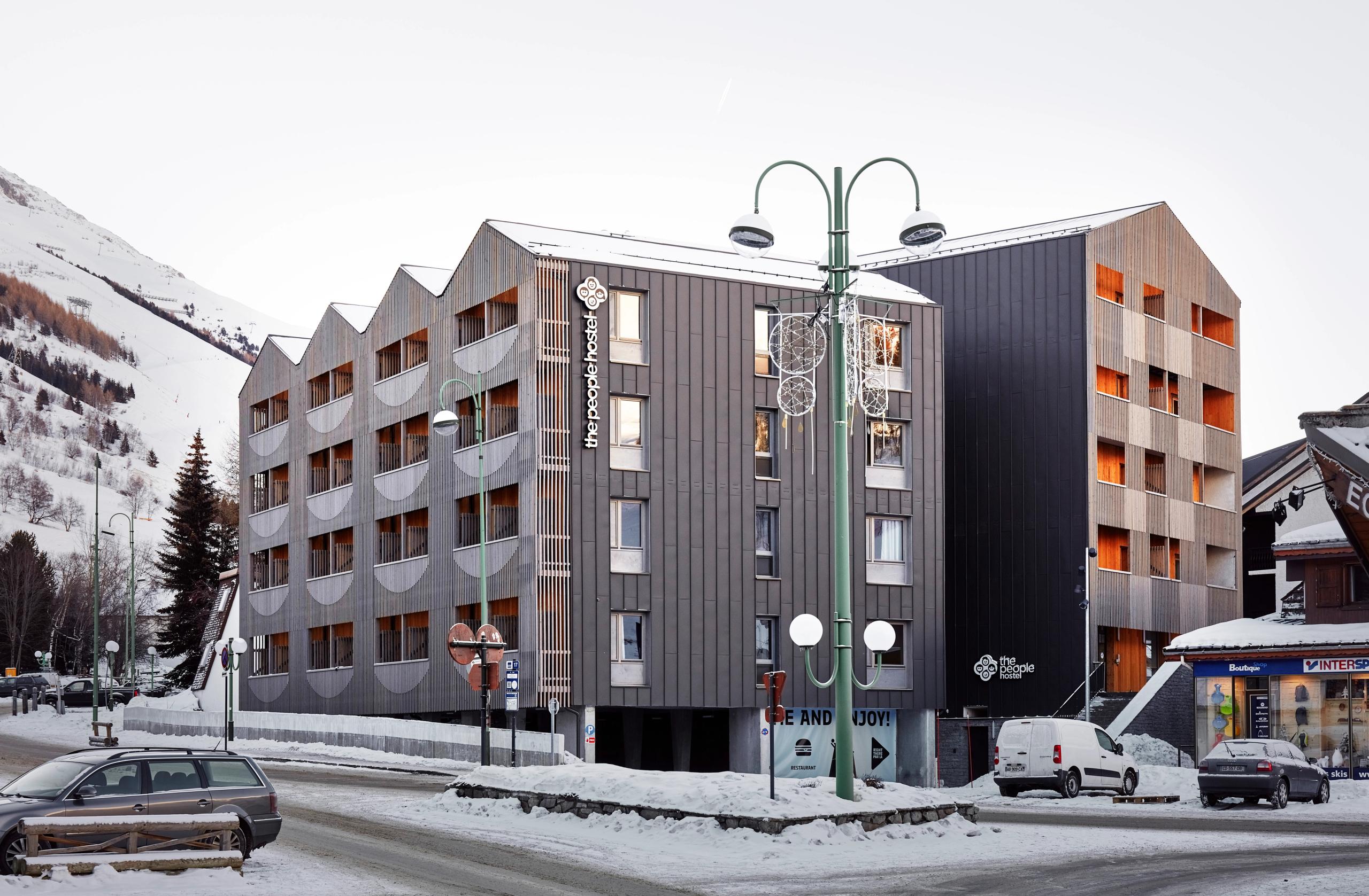 Réhabilitation et extension de l’auberge de jeunesse The People Hostel aux Deux Alpes, volumes fragmentés en CLT, façades bois et métal à claire-voie en pied de station.