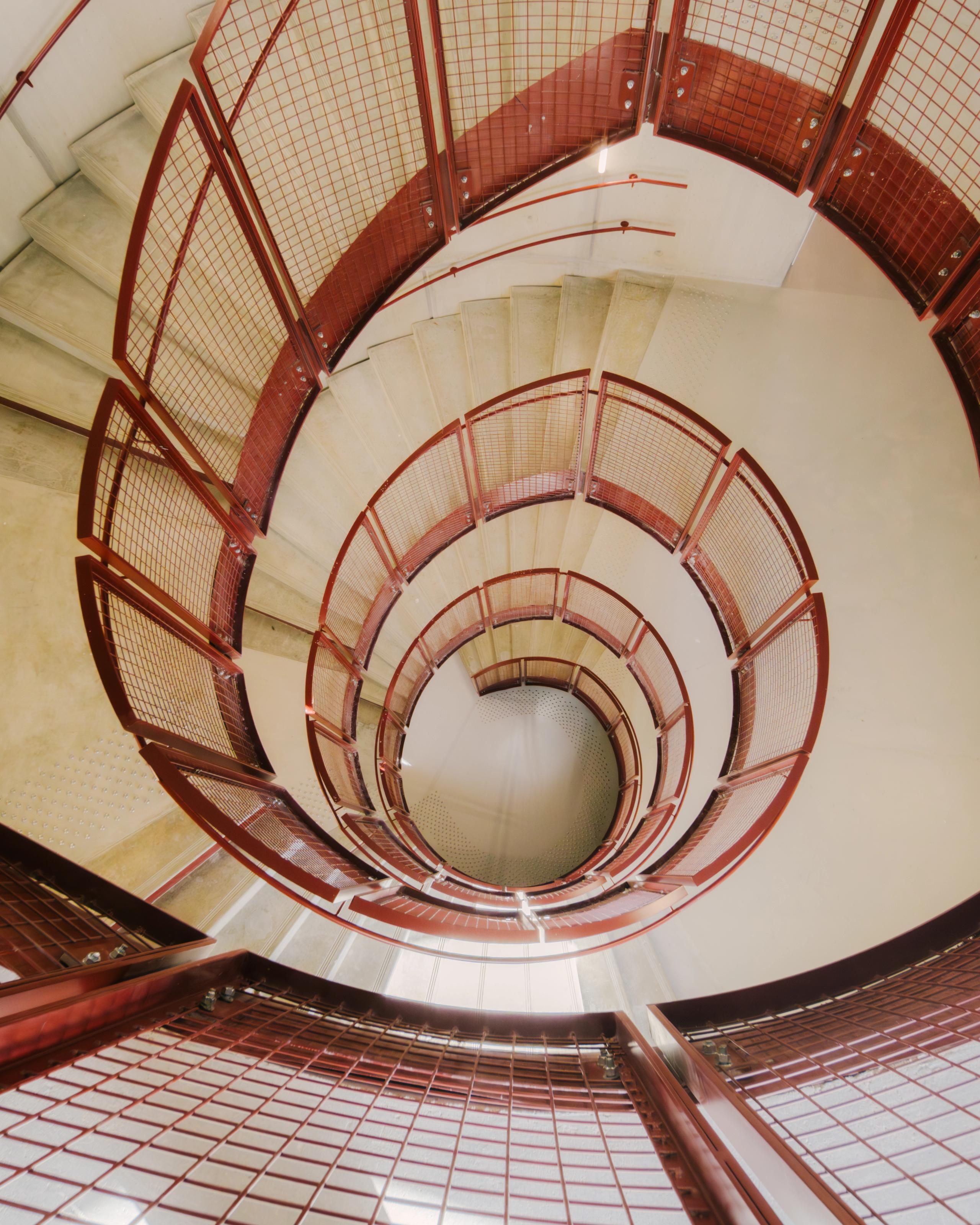 Escalier hélicoïdal du groupe scolaire Dominique Frelaut à Colombes, structure béton et garde-corps métalliques rouges formant un puits central lumineux.