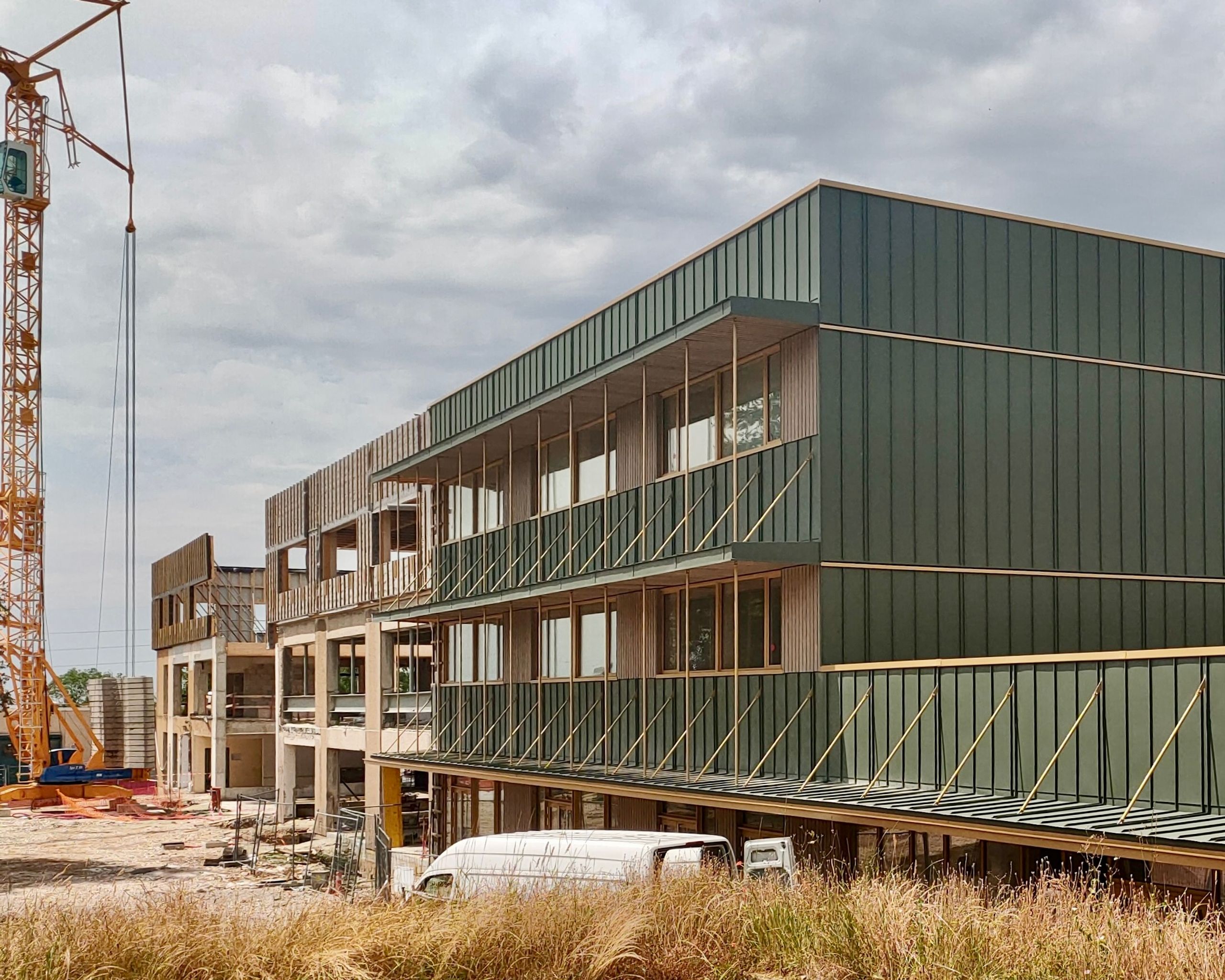 Chantier de restructuration du collège Maryse Bastié à Dole : volumes R+2 en ossature bois et bardage métallique vert, structure béton existante partiellement ouverte.