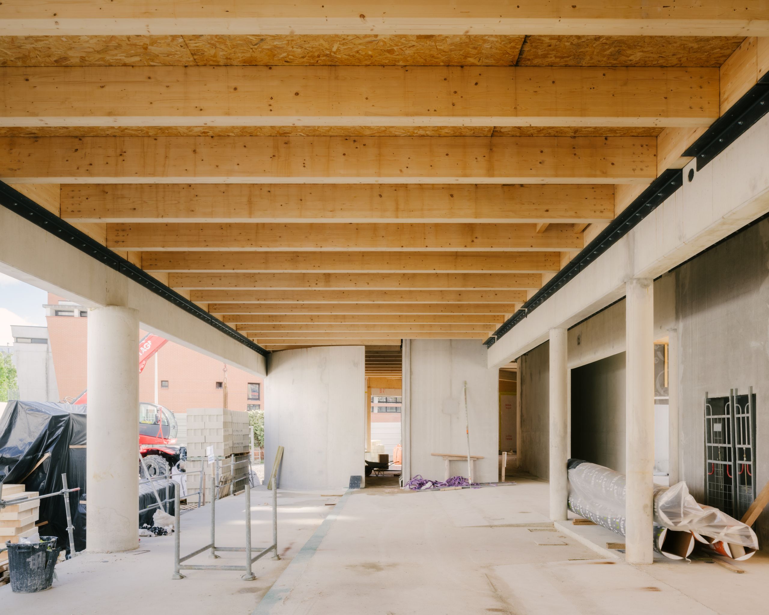 Chantier du Groupe scolaire Dominique Frelaut à Colombes : galerie couverte en structure mixte béton-poteaux ronds et plafond à poutres bois apparentes.