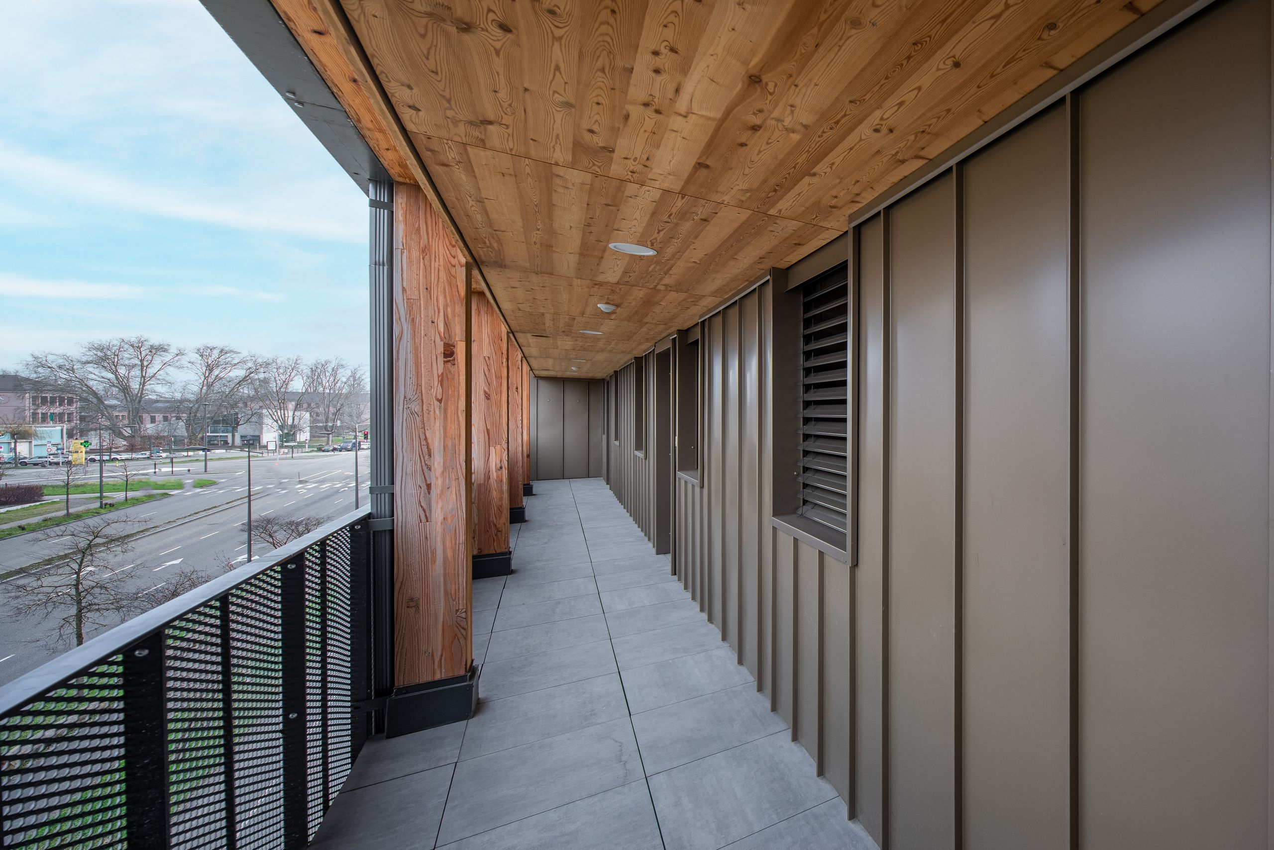 Coursive extérieure des 98 logements à Strasbourg par Tectoniques, structure bois, parement métallique et garde-corps perforé sur rue urbaine.