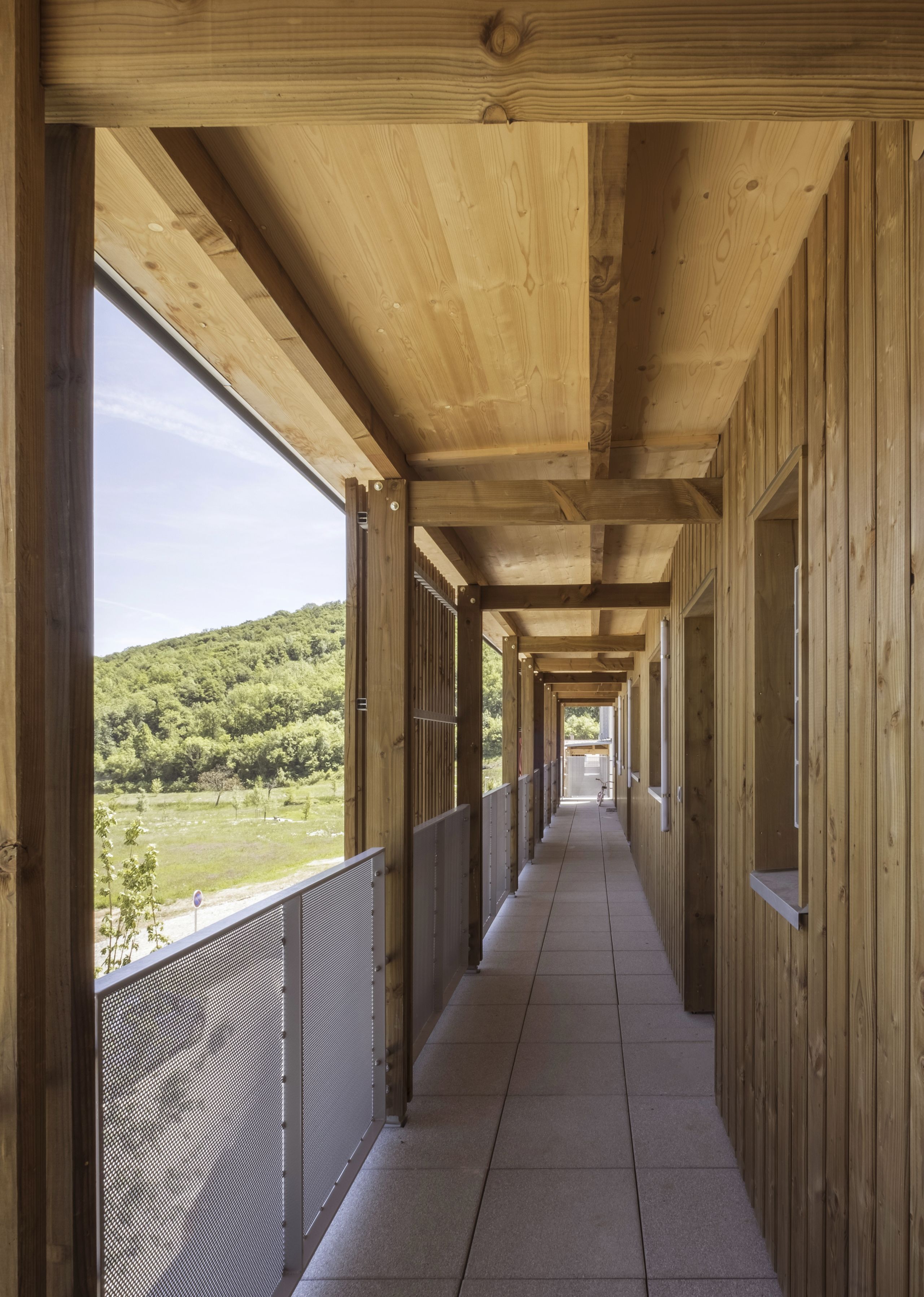 Coursive extérieure en bois des 65 logements à Seyssins, structure poteaux-poutres, garde-corps métalliques perforés, ouverte sur le paysage du Vercors.