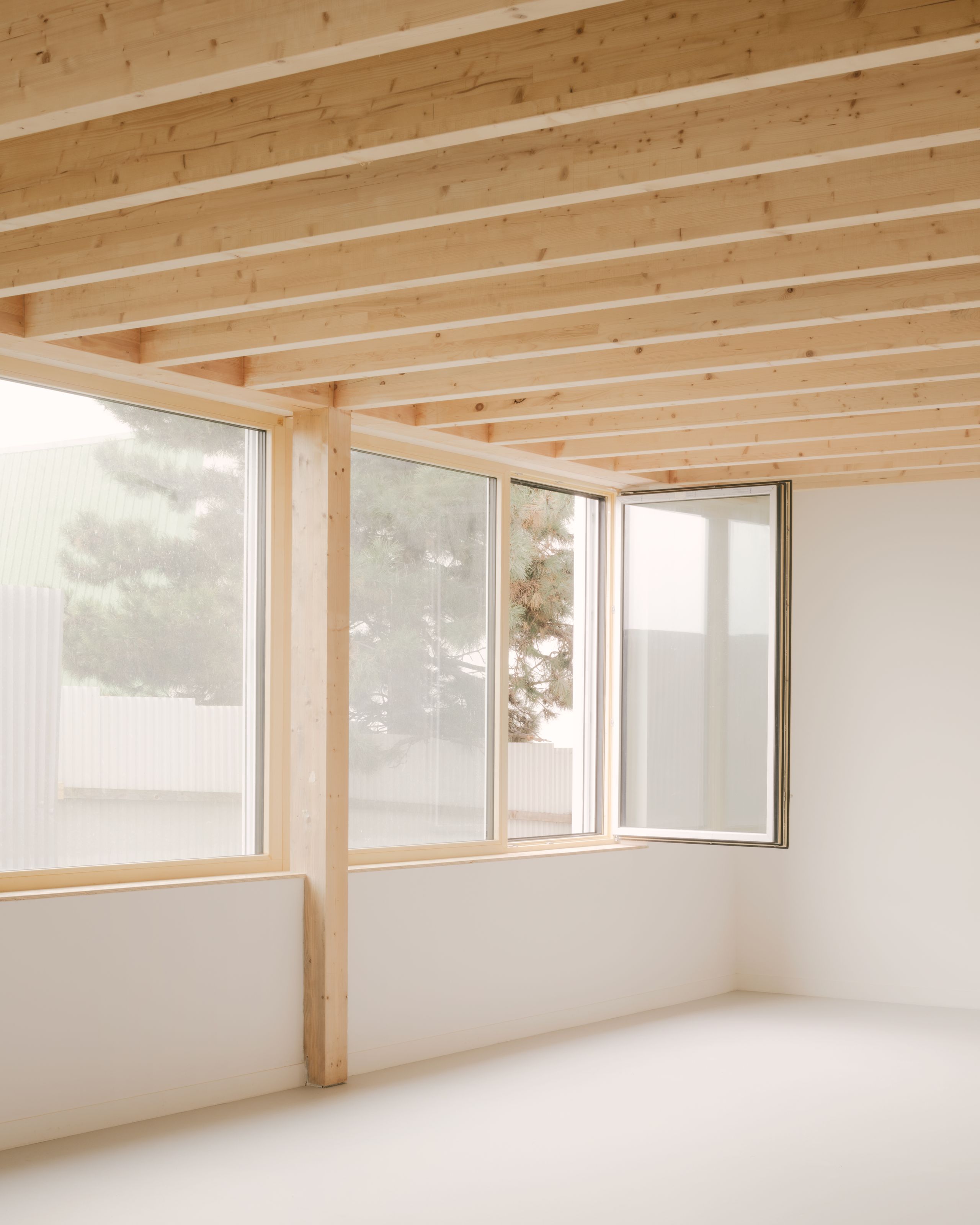 Intérieur des groupes scolaires Jacqueline Auriol et Jean Jaurès au Bourget, avec structure bois apparente et grandes baies vitrées ouvrant sur le parc.