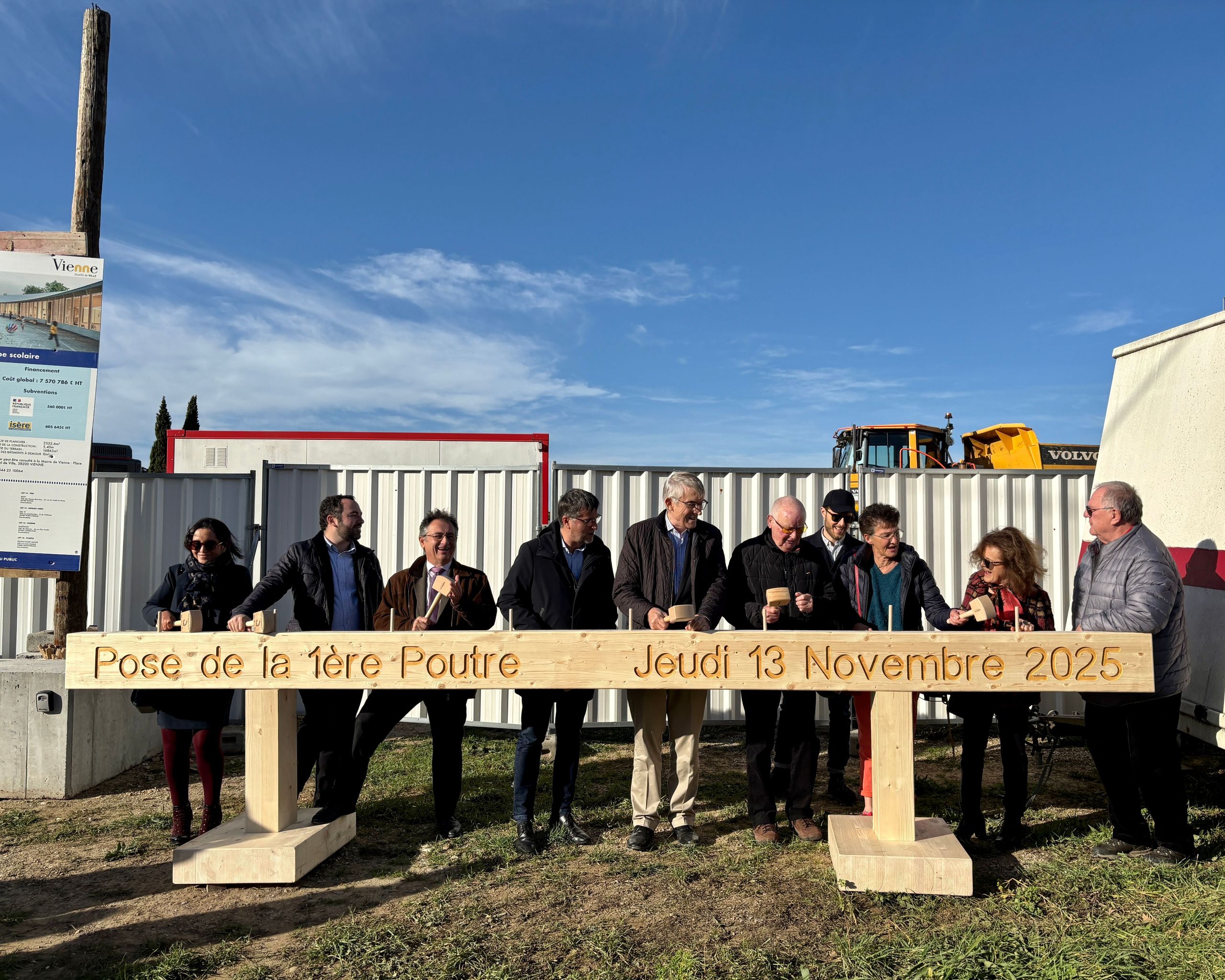 Cérémonie de pose de la première poutre en bois du groupe scolaire de Vienne, élus et maîtrise d’ouvrage alignés devant le chantier et les engins de terrassement.