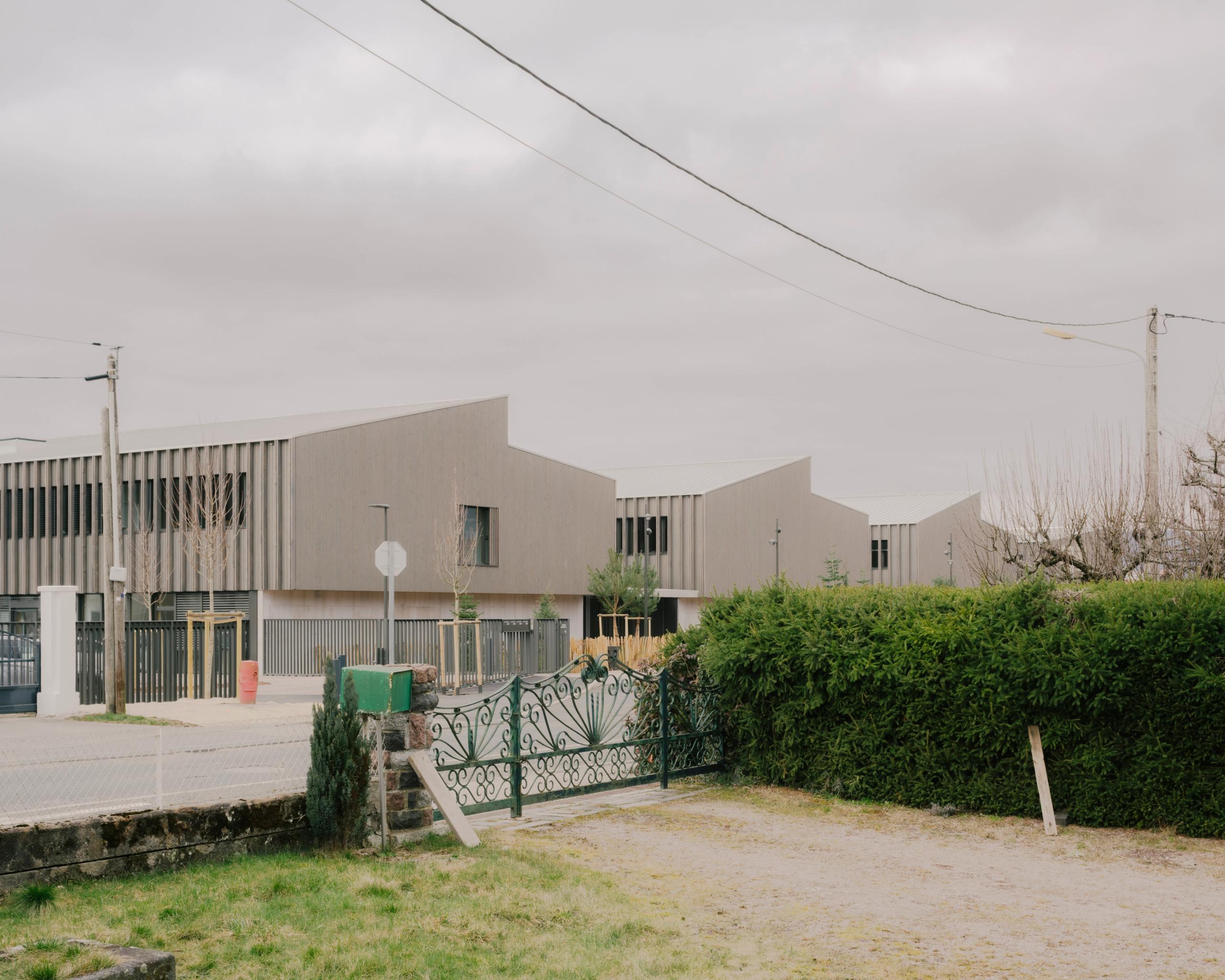 Vue lointaine du Collège du Ban à Vagney : volumes en peigne à toitures inclinées, façades bois rythmées de lames verticales, insérés dans le tissu pavillonnaire.