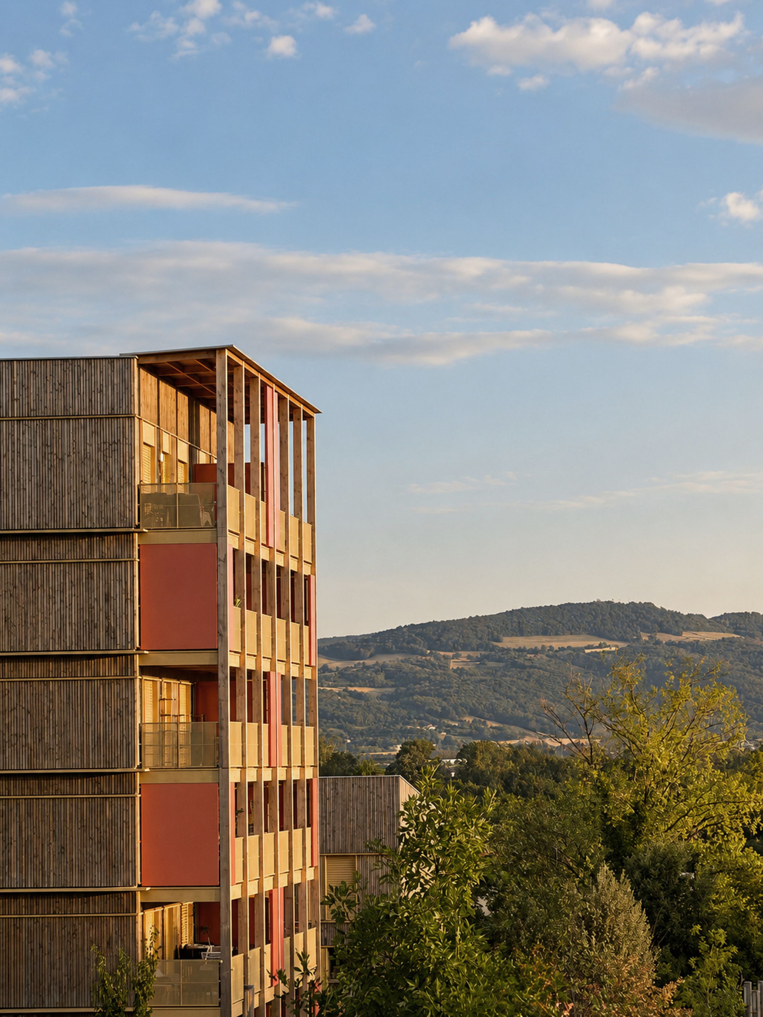 84 logements à Trévoux : façades à ossature et exo-structure bois, balcons et panneaux colorés ouverts sur le paysage vallonné.