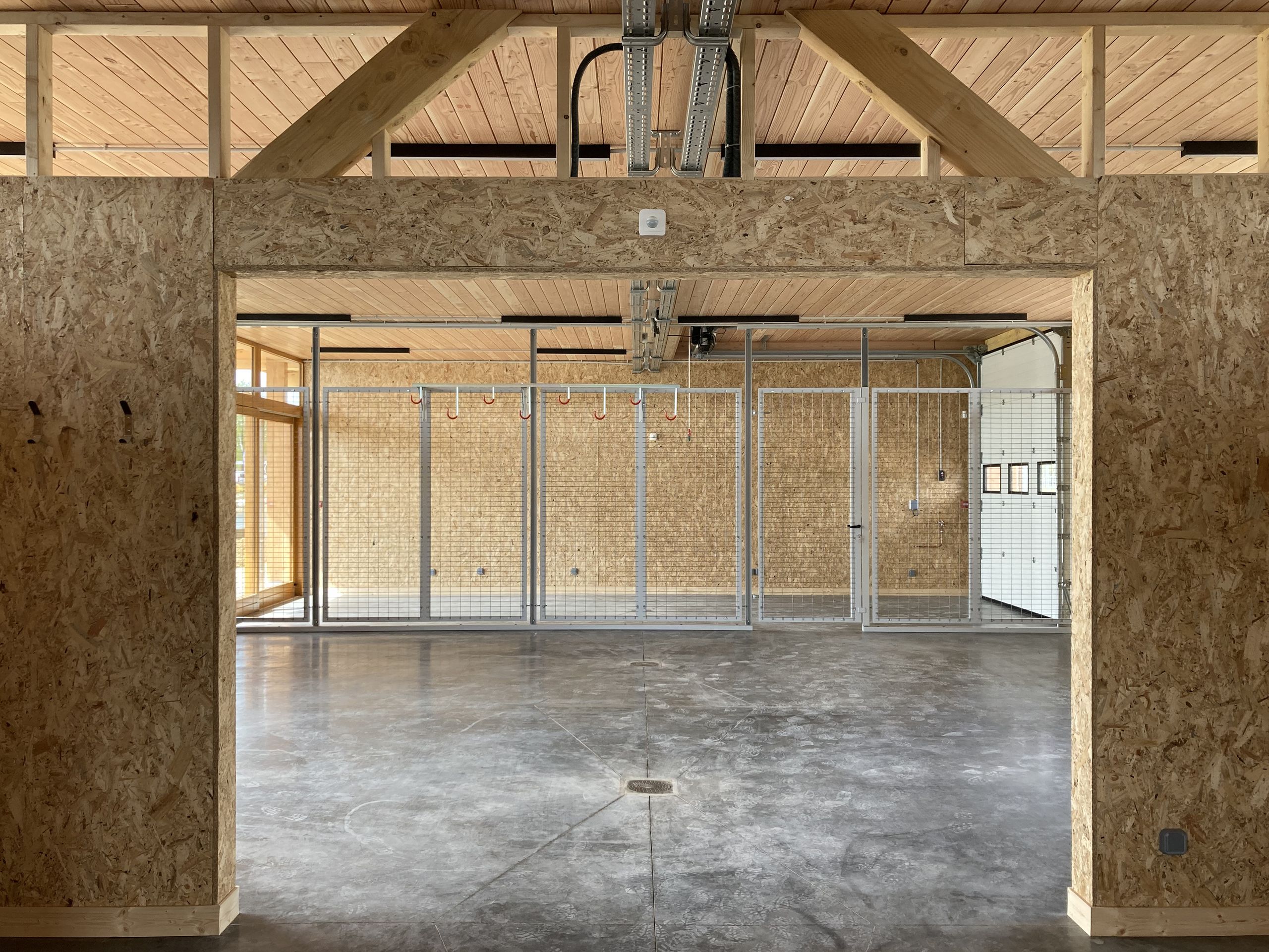 Intérieur de la Maison des sports à Malafretaz, grand volume traversant en ossature bois et OSB, plancher béton brut et cloisonnements métalliques ajourés.