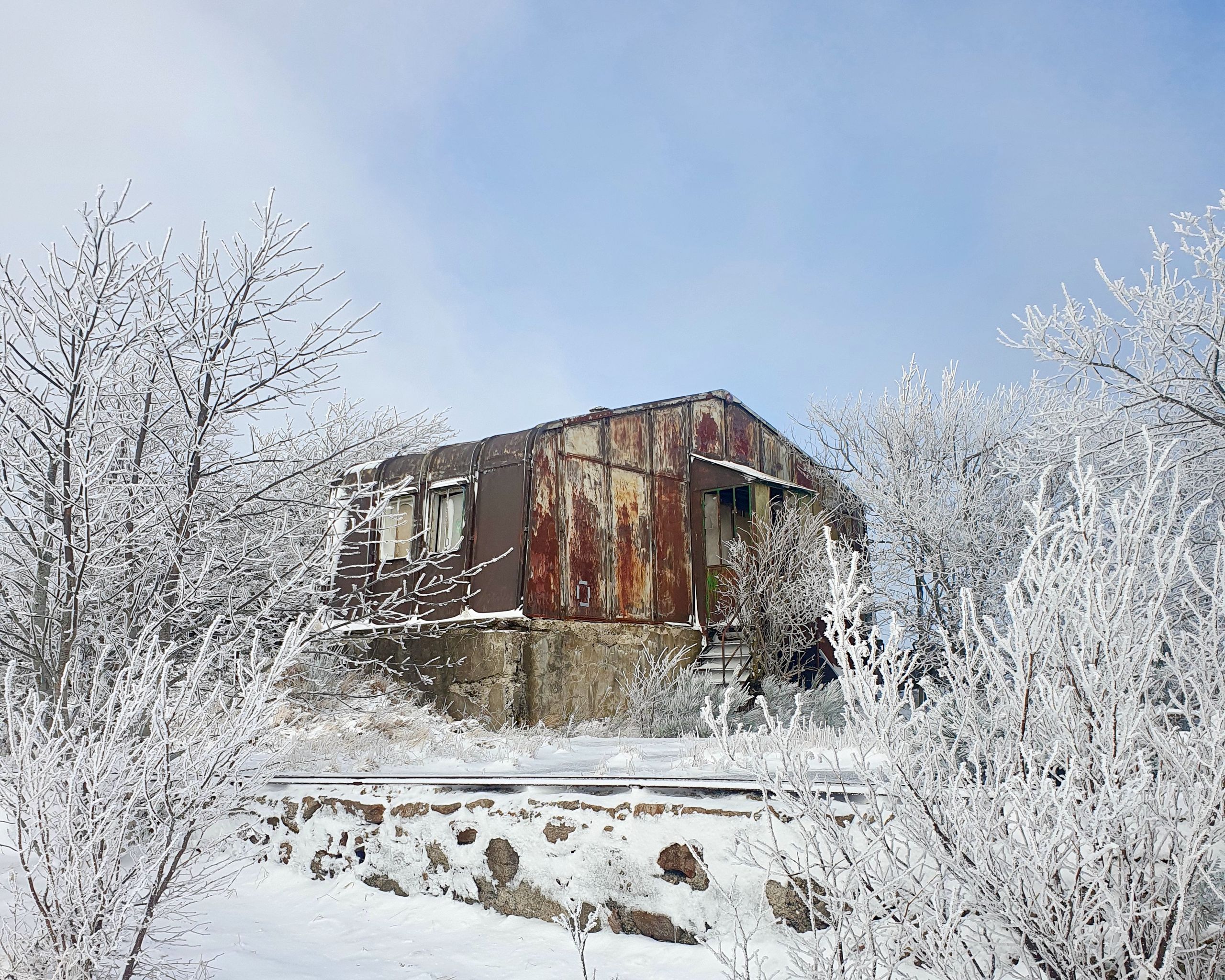 Vue de l’ancienne auberge métallique du col de l’Oeillon à Véranne, volume compact et oxydé posé sur un socle en pierre, isolé dans un paysage enneigé.