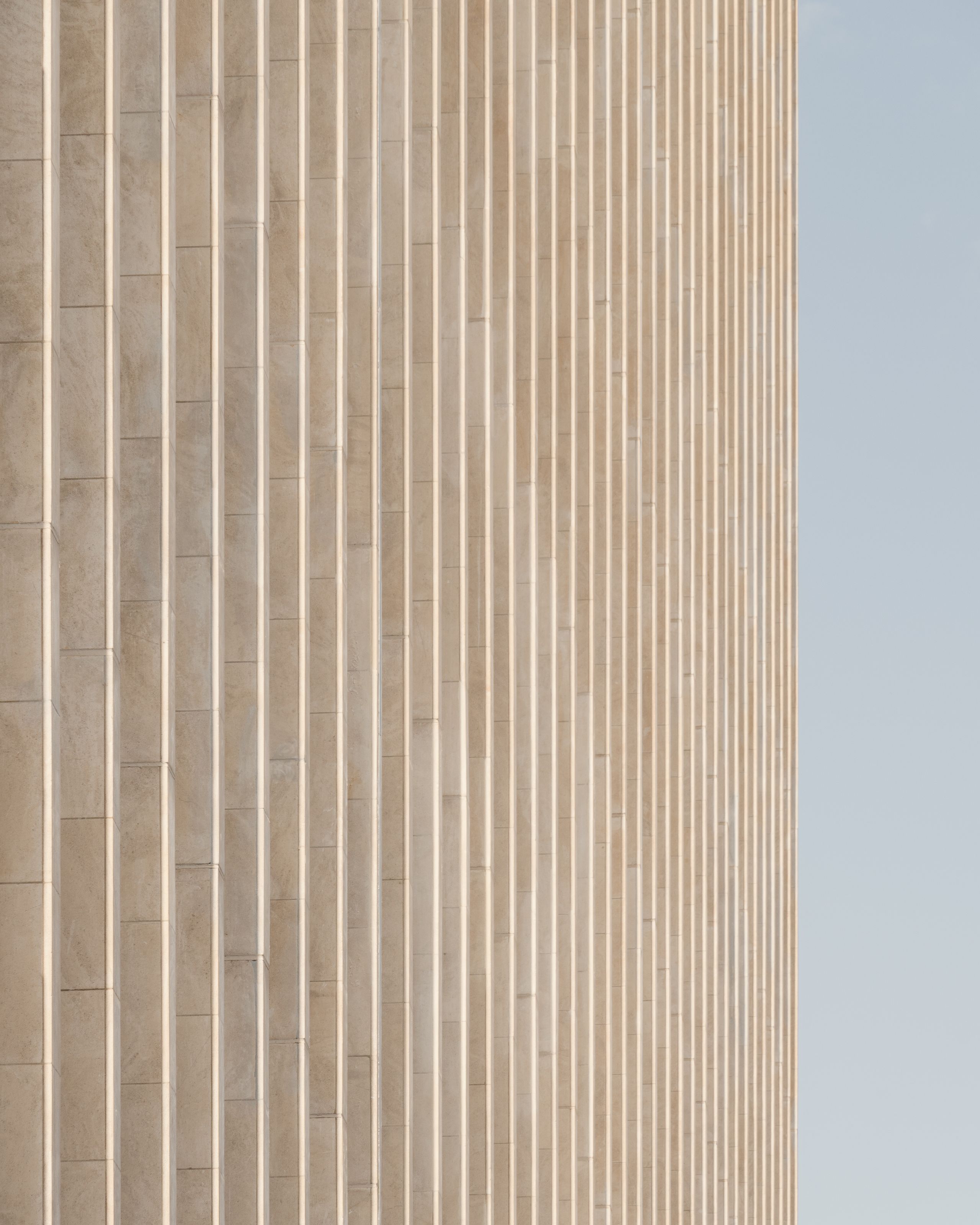 Façade rythmée de l’IGH Émile Loubet à Saint-Étienne, parement minéral clair à lames verticales régulières, révélant la trame structurelle existante.