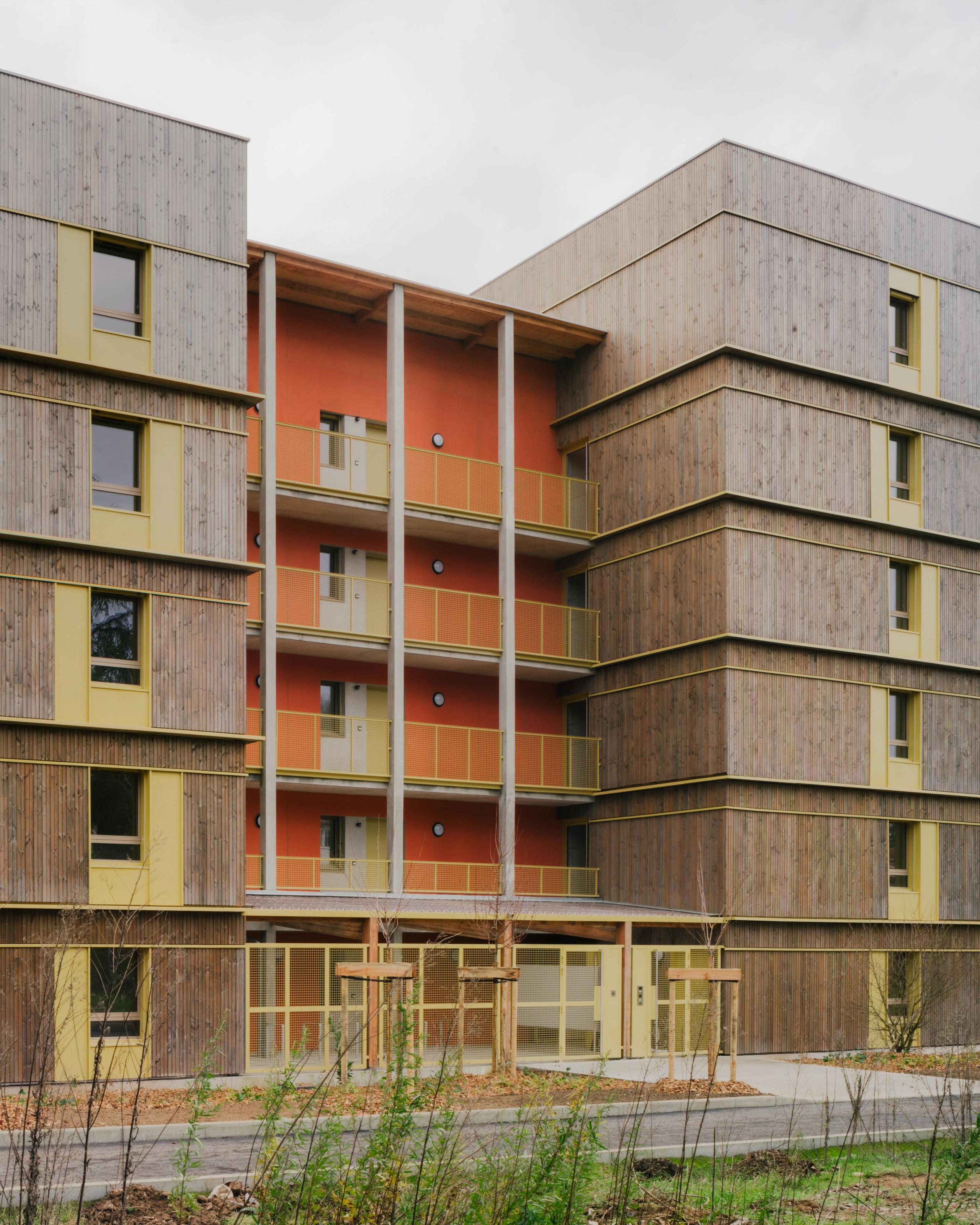 Façade des 84 logements à Trévoux par Tectoniques, volumes en gradins bois-béton, coursives extérieures colorées et exo-structures bois en lisière de parc.