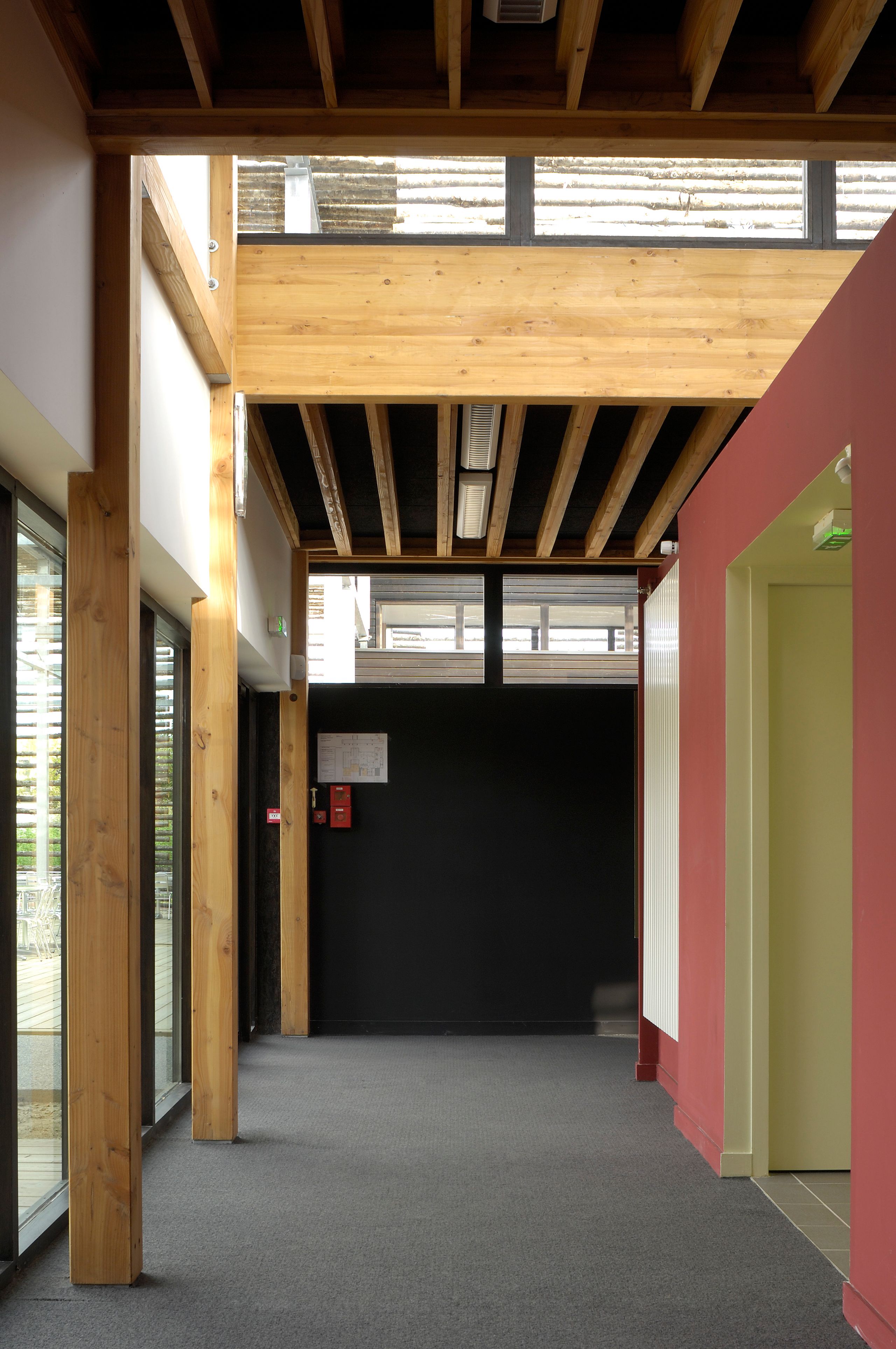 Circulation du restaurant administratif de Bron par Tectoniques, structure bois apparente, façade vitrée sur terrasse et volumes intérieurs colorés.