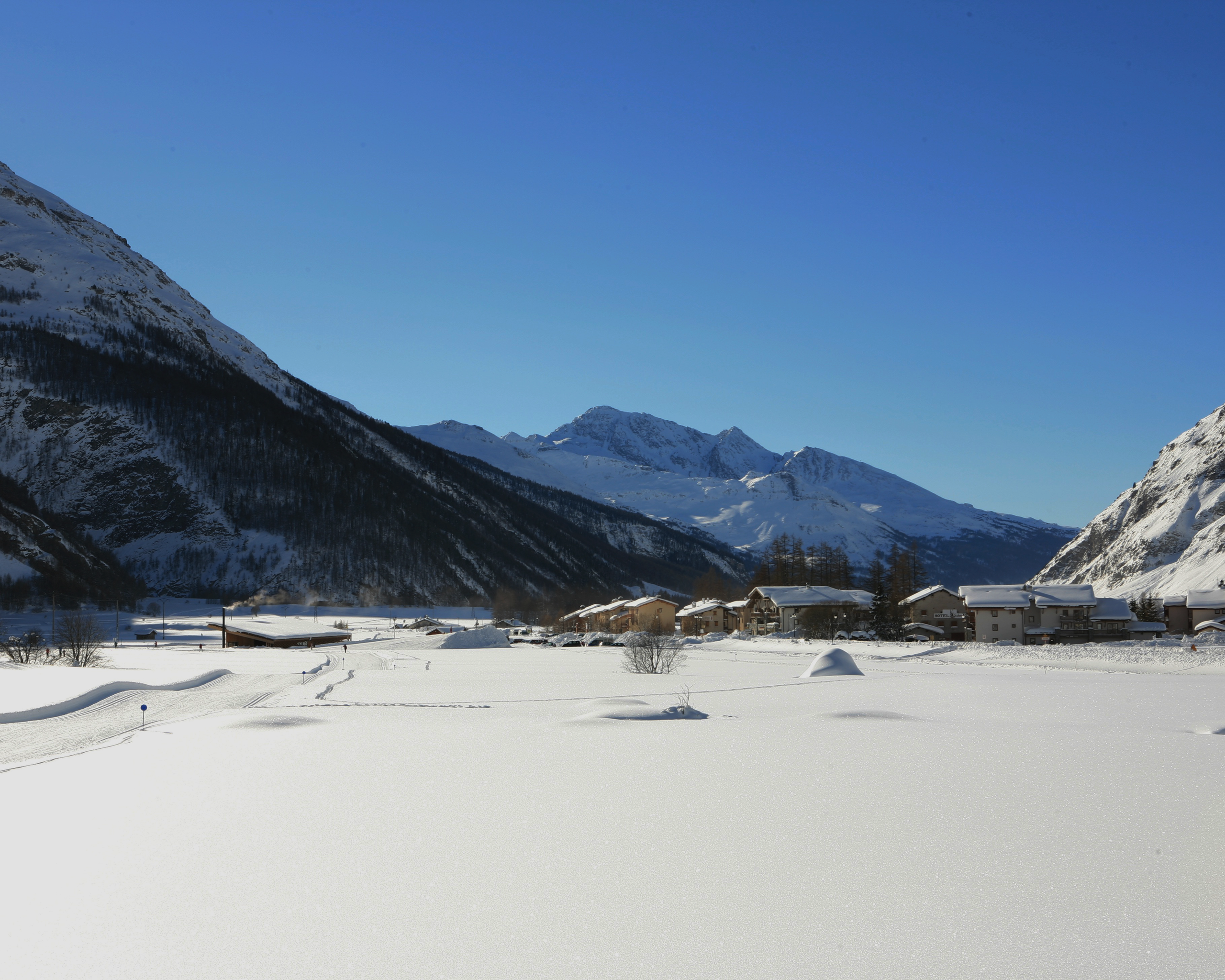 Espace nordique de Bessans, volume bas en bois et lauze grise en lisière du village, face aux pistes de ski de fond dans le paysage ouvert de Haute-Maurienne.