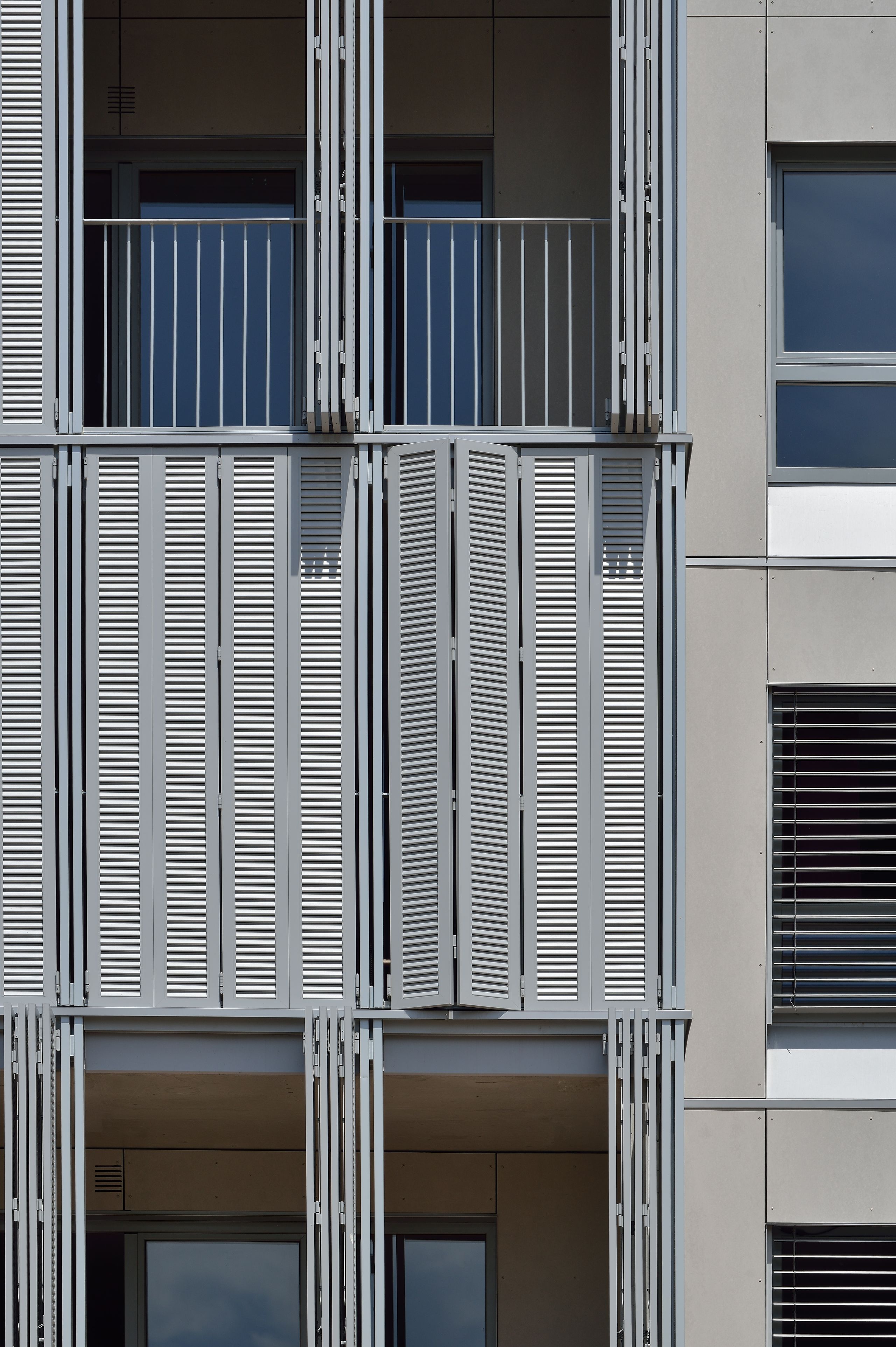 Façade des 28 logements à Villeurbanne, loggias superposées avec persiennes métalliques coulissantes et garde-corps fins, cadrant les baies vitrées.