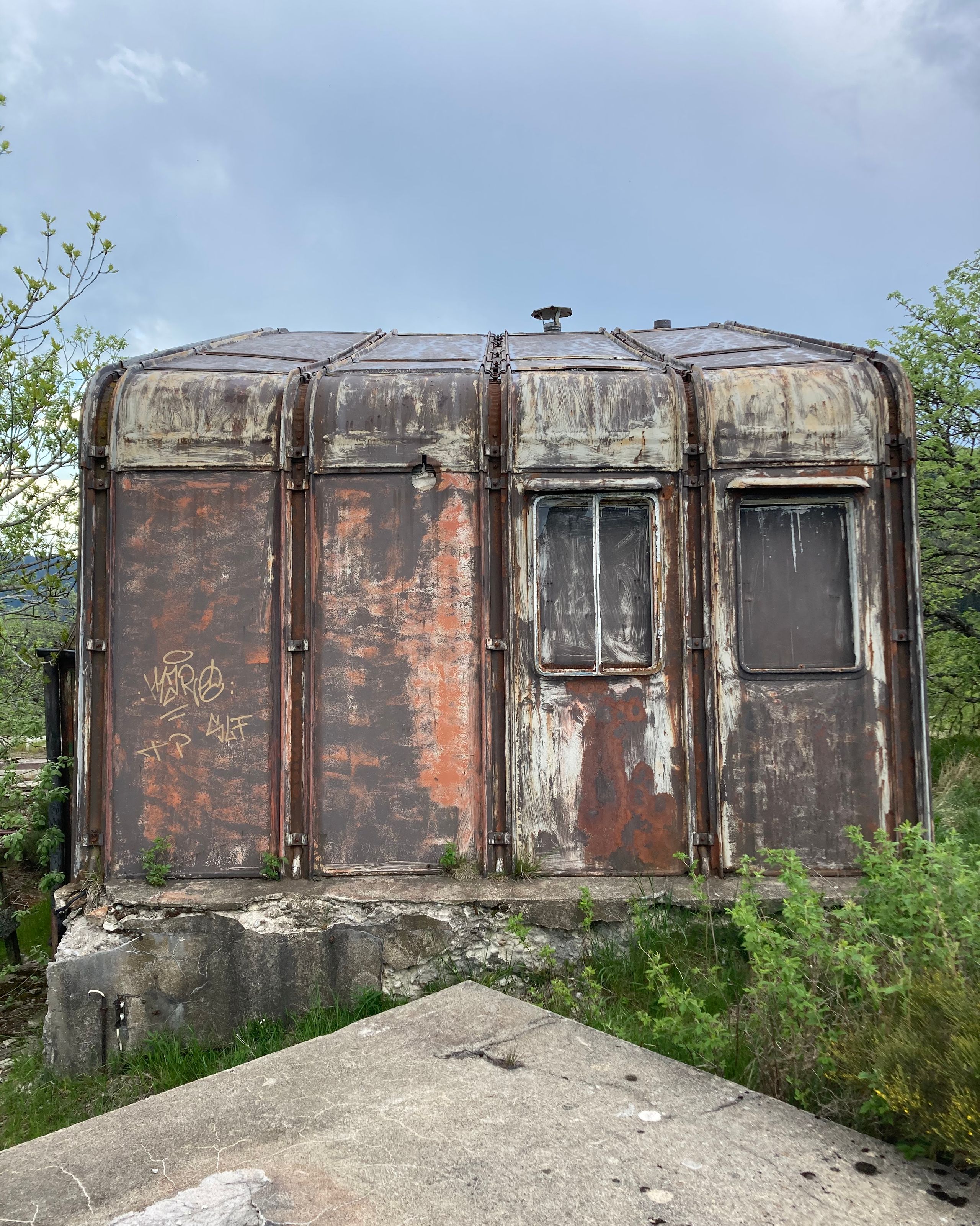 Vue rapprochée du module métallique de Ferdinand Fillot au col de l’Oeillon à Véranne, enveloppe rivetée oxydée sur socle béton, avant restauration en bar d’altitude.