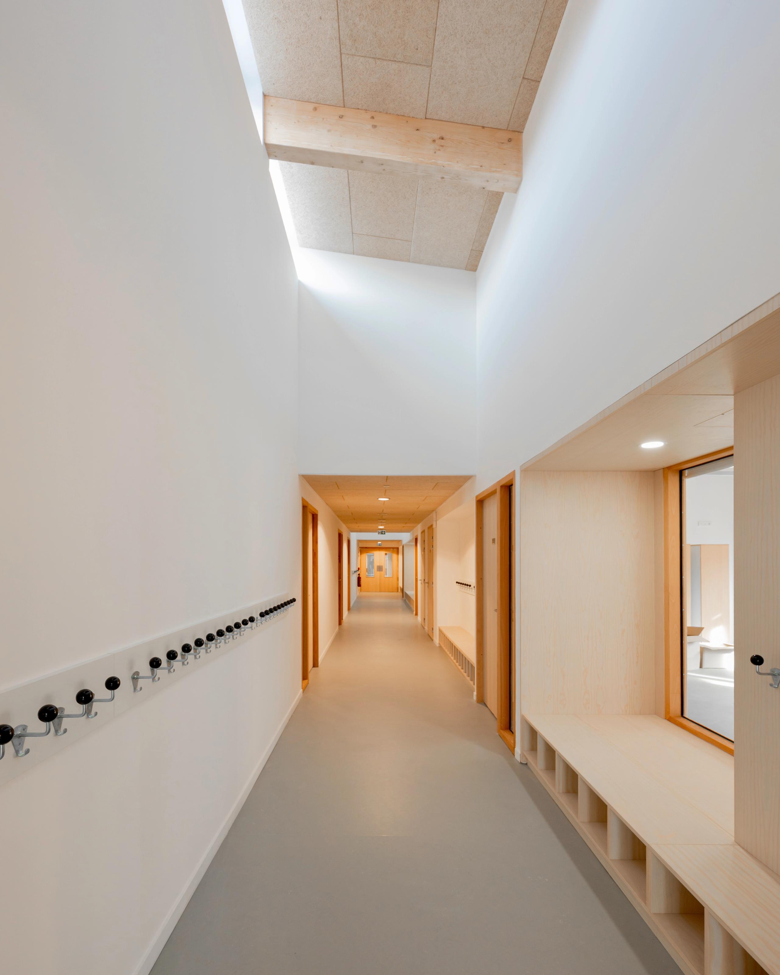 Couloir du groupe scolaire du Bouchet à Bonneville, éclairé zénithalement, finitions bois clair et rangements intégrés, illustrant la restructuration intérieure.