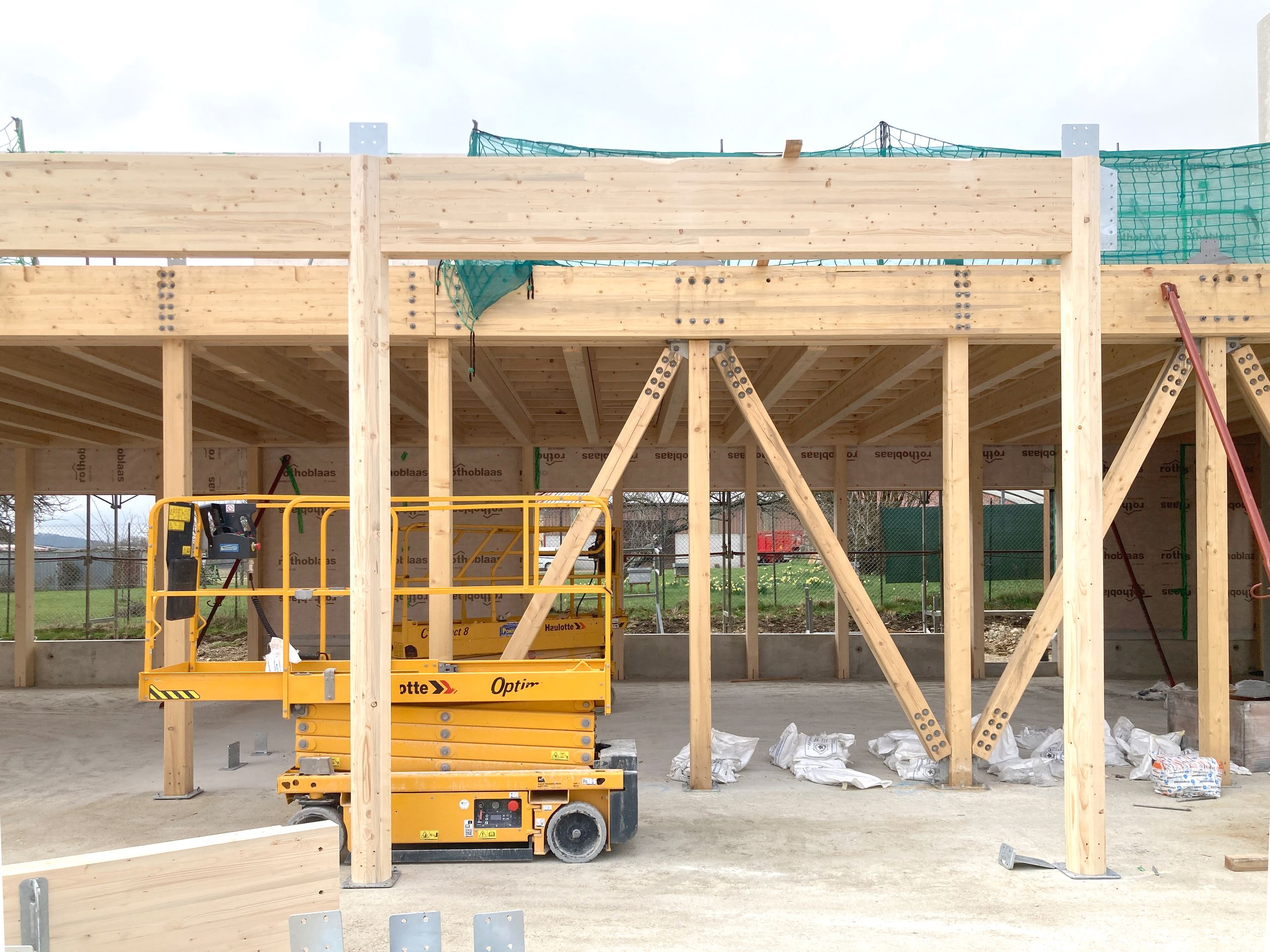 Chantier du groupe scolaire Louis Pergaud à Levier : structure bois apparente, poteaux-poutres et contreventements, plan libre de la future cour couverte.