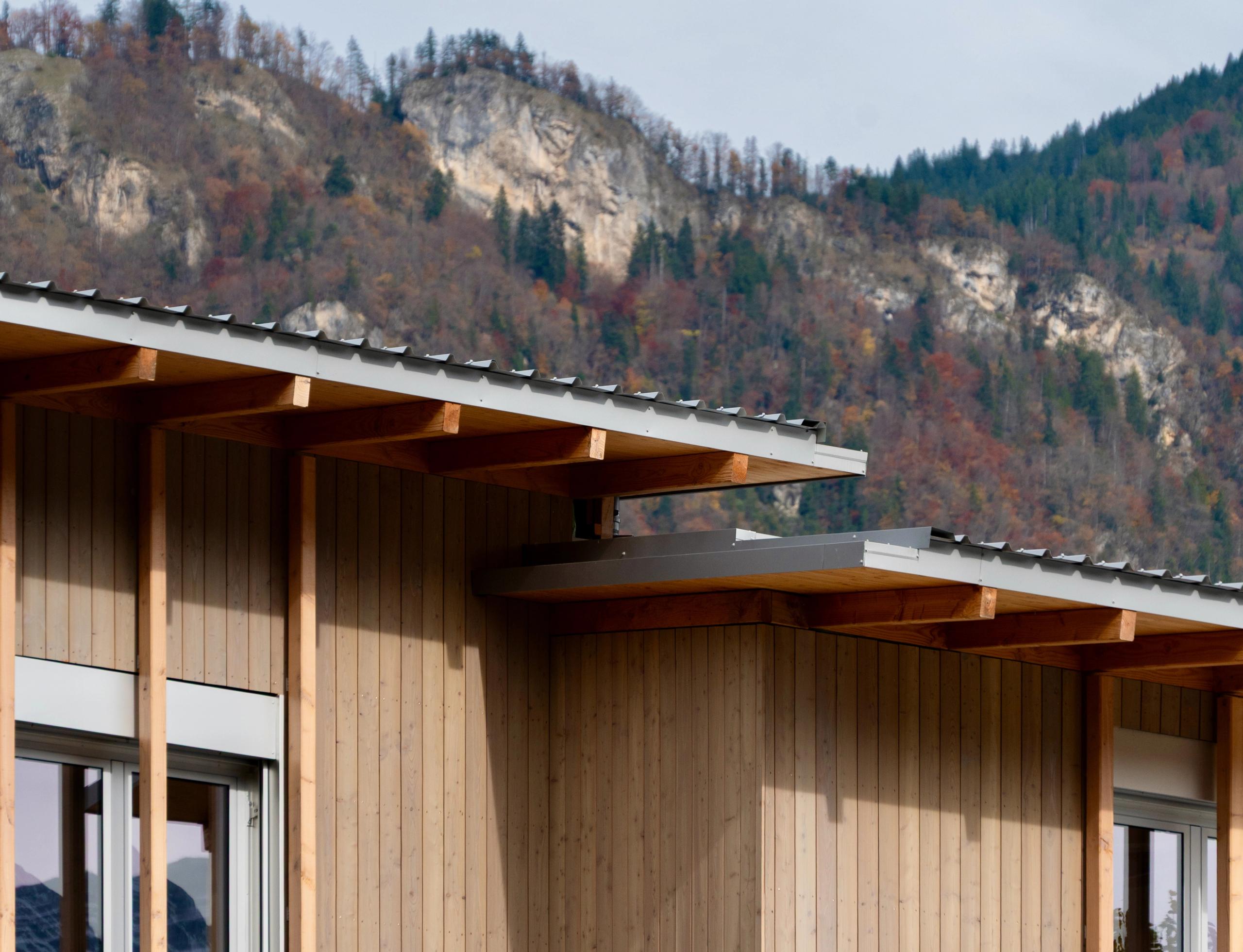 Façade en ossature bois surélevée du School complex du Bouchet à Bonneville, toitures métalliques décalées devant le relief montagneux boisé.