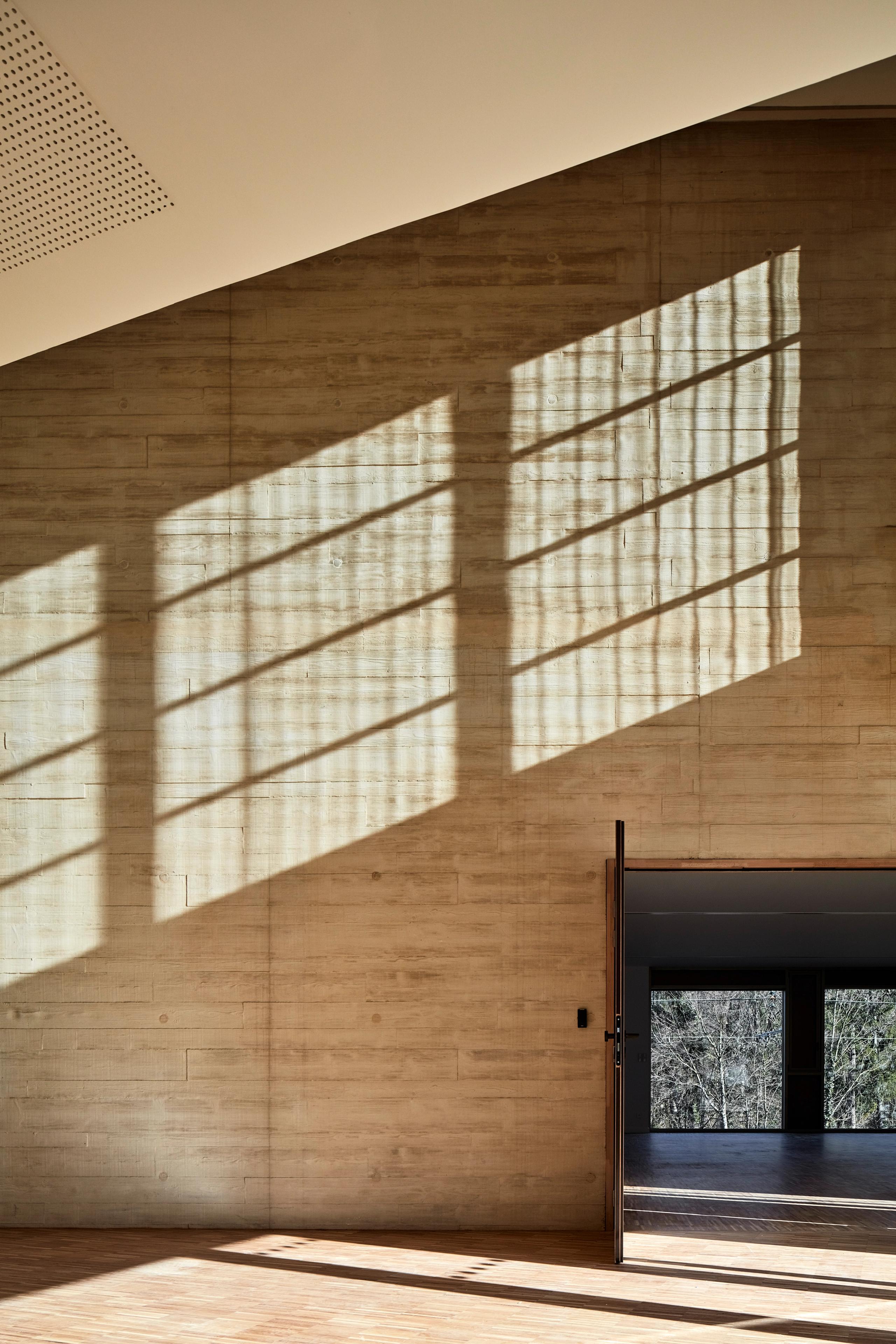 Interior view of Maison des Arts in Charbonnières-les-Bains, showing tiled circulation space with benches and hooks framed by a textured timber wall.