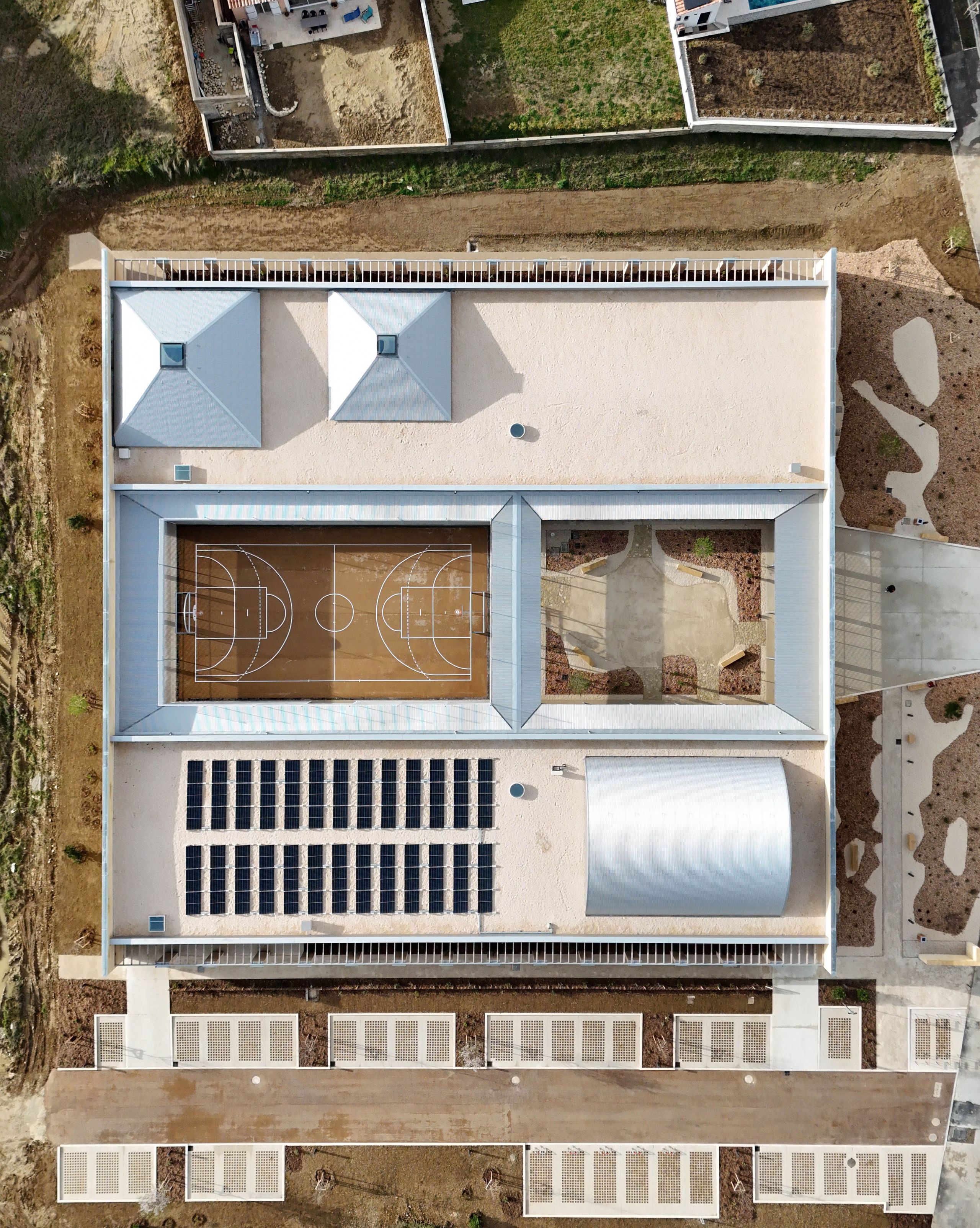 Vue aérienne du pôle culture et jeunesse de Vaison-la-Romaine : enceinte carrée en pierre, ailes basses encadrant jardin central et city stade, toitures équipées de panneaux solaires.