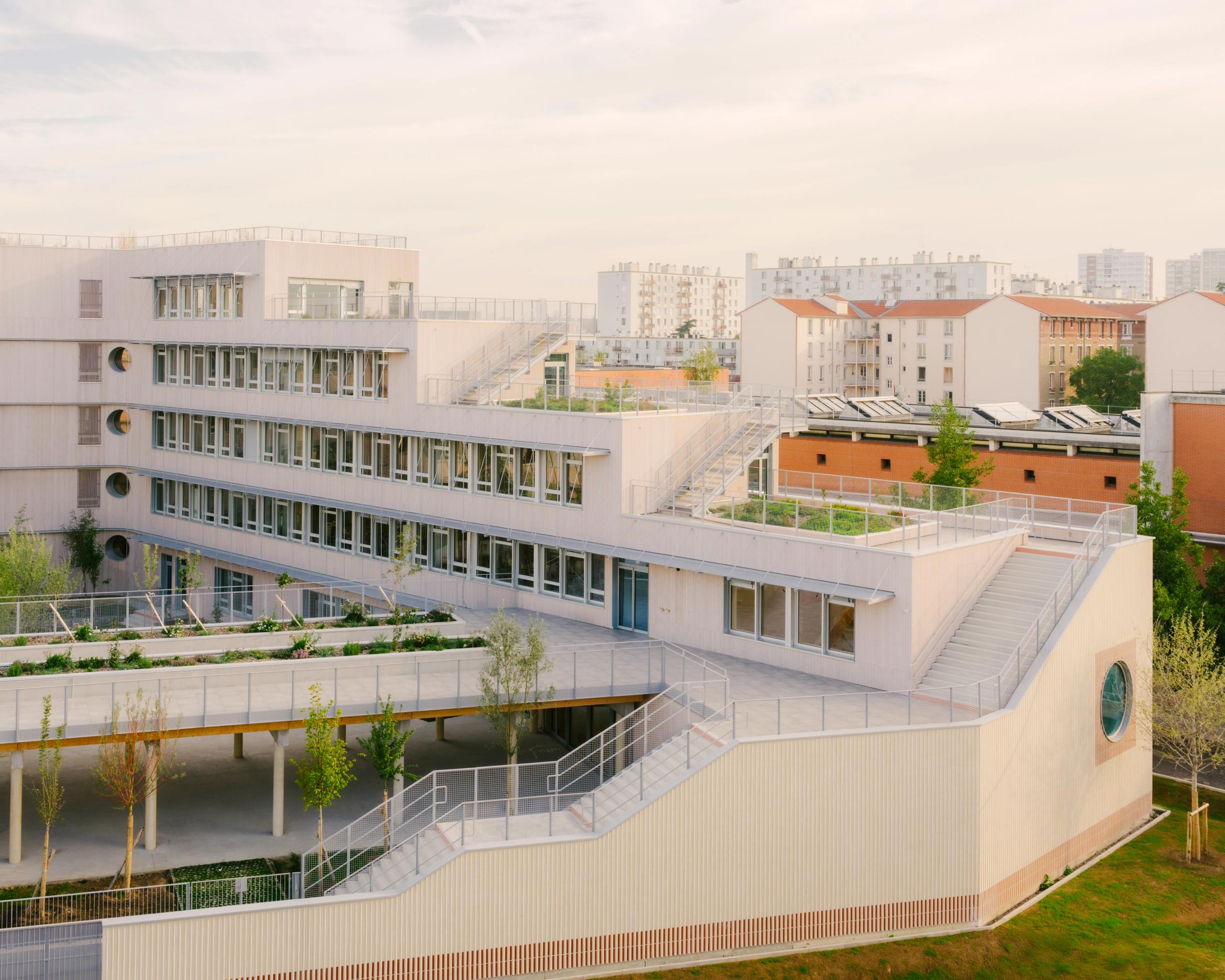 Vue du Groupe scolaire Dominique Frelaut à Colombes : volumes en gradins en U, façades claires largement vitrées, terrasses plantées et circulations extérieures en rampe.