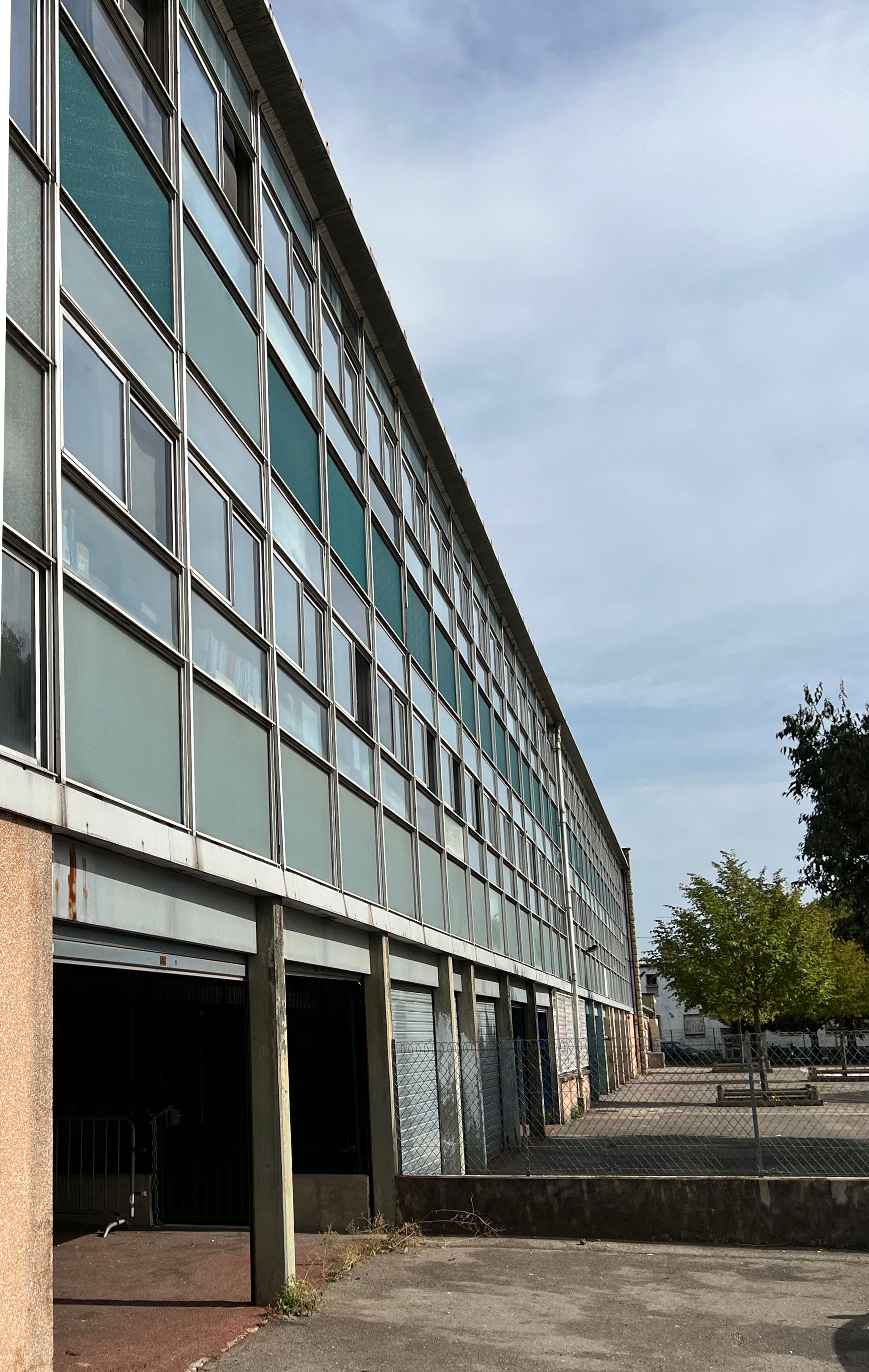 Façade existante du groupe scolaire Kennedy à Lyon, long bâtiment faubourien vitré et répétitif, ouvrant sur une cour minérale en attente de restructuration.