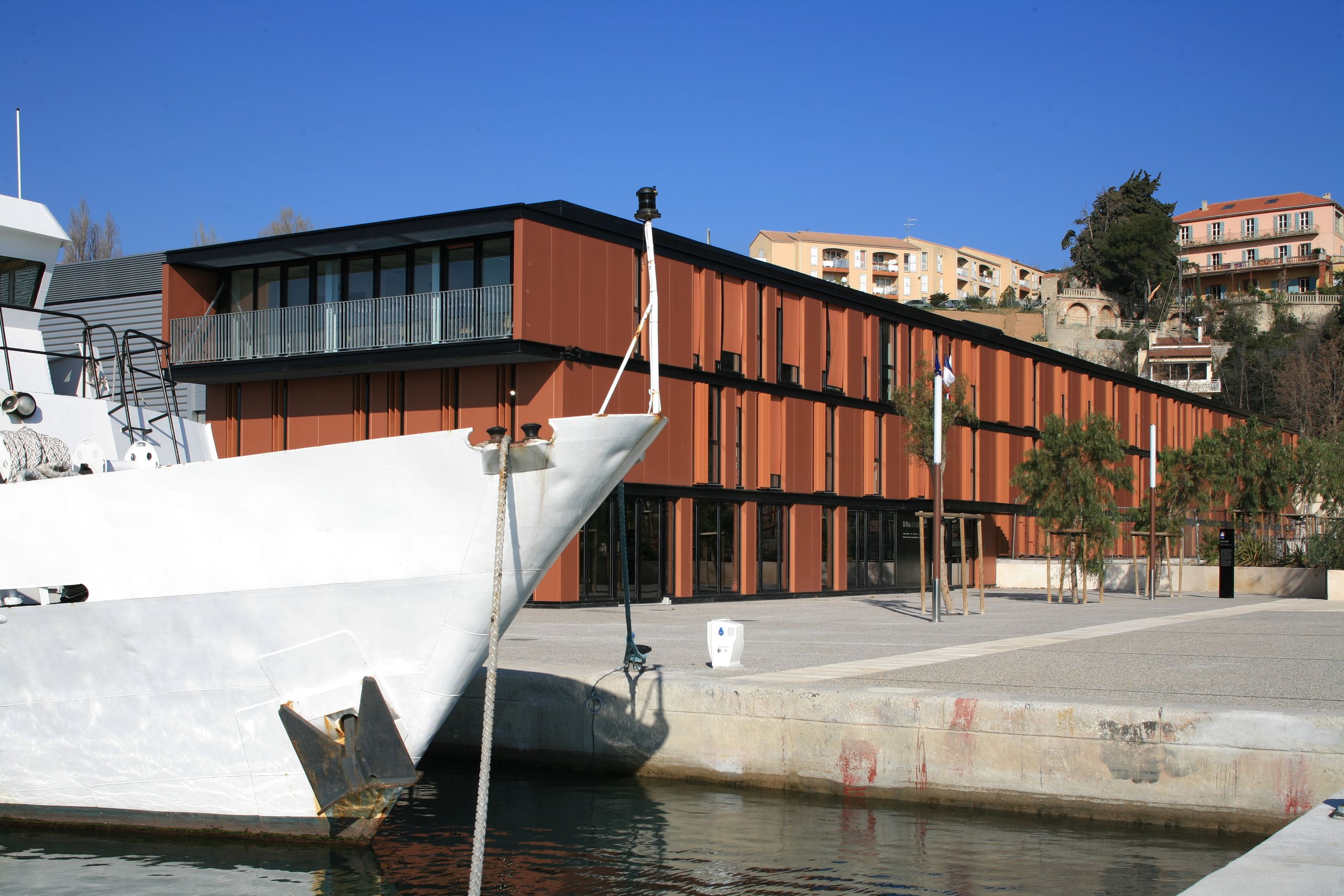 Façade en bardage métallique rouille du Département des Recherches Subaquatiques et Sous-Marines à Marseille, en front de quai, face à un navire blanc.