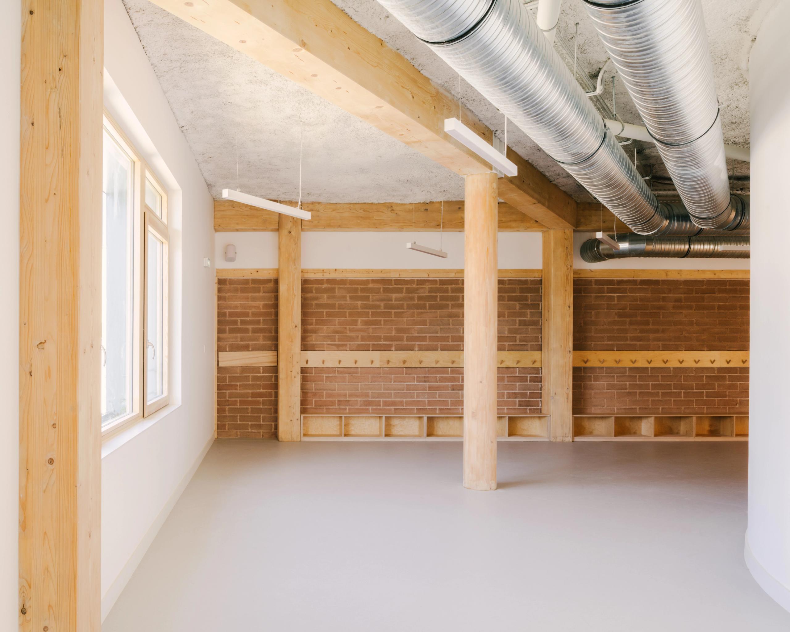 Intérieur du Groupe scolaire Dominique Frelaut à Colombes : espace en structure bois, murs en brique, plafond technique apparent et lumière naturelle latérale.