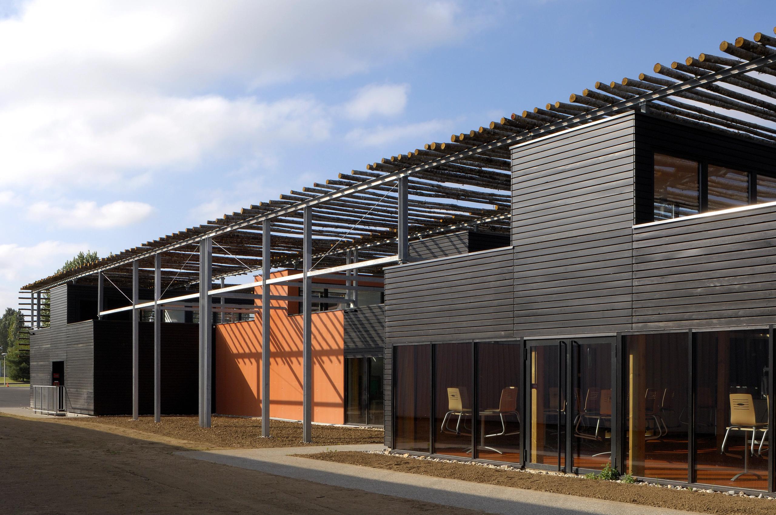 Restaurant administratif du CETE à Bron, volumes modulaires bardés de bois sombre sous ombrière en baliveaux de châtaignier, terrasses et façades vitrées.
