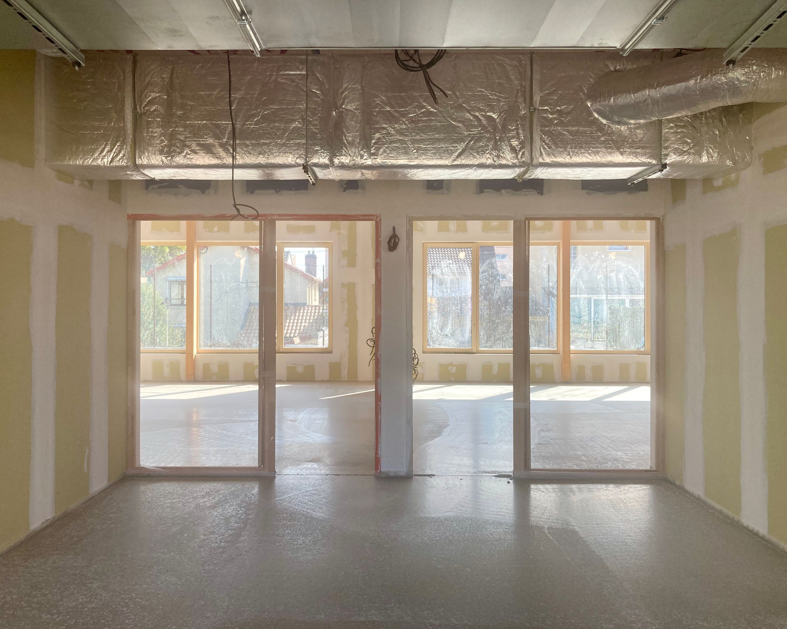 Vue intérieure en chantier des groupes scolaires Jacqueline Auriol et Jean Jaurès au Bourget, avec cloisonnement sec, gaines apparentes et larges baies vitrées sur cour.