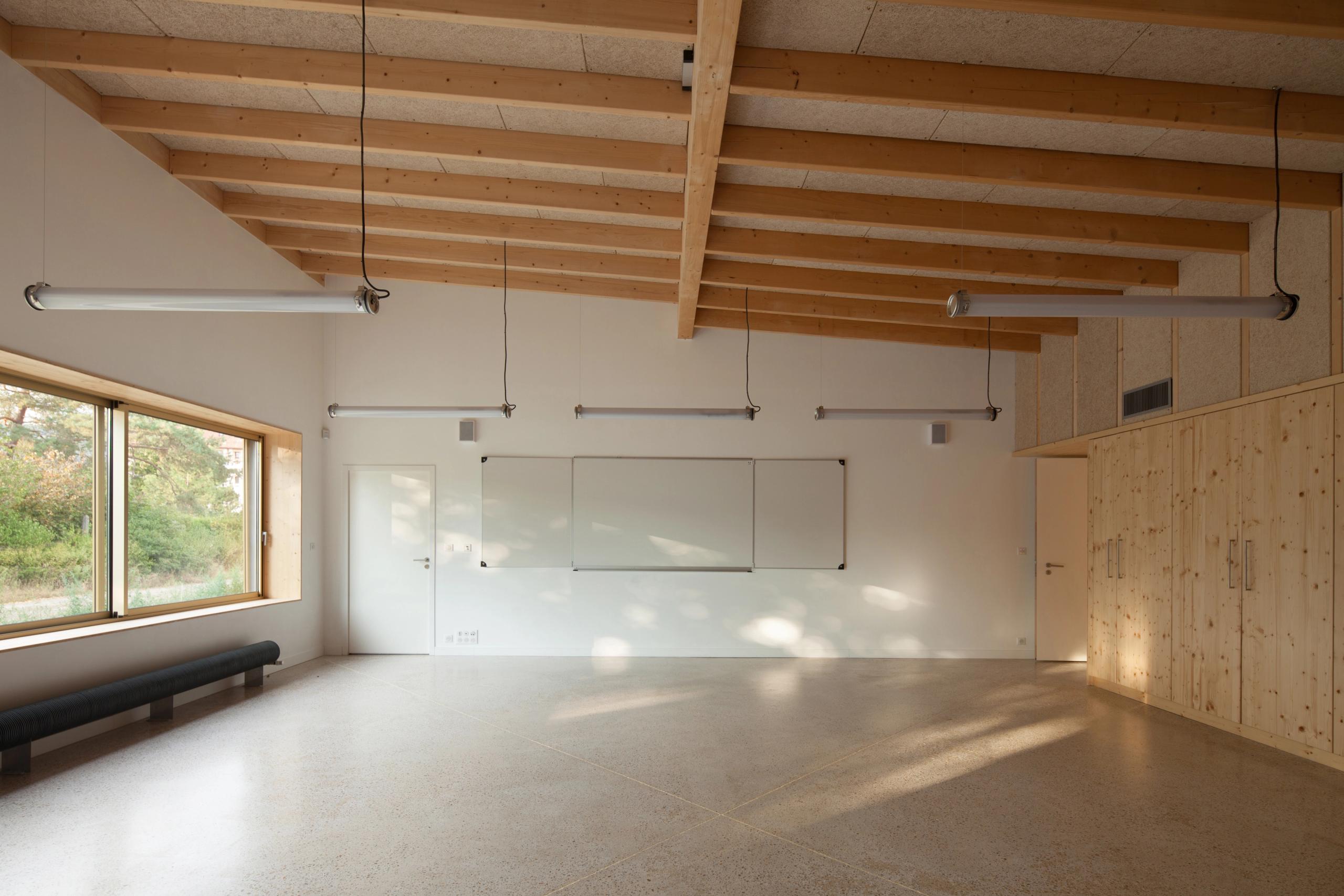 Salle de classe de l’école élémentaire Hubert Reeves à Champagnole, ossature bois apparente, grandes baies vitrées, rangements intégrés et sol minéral clair.