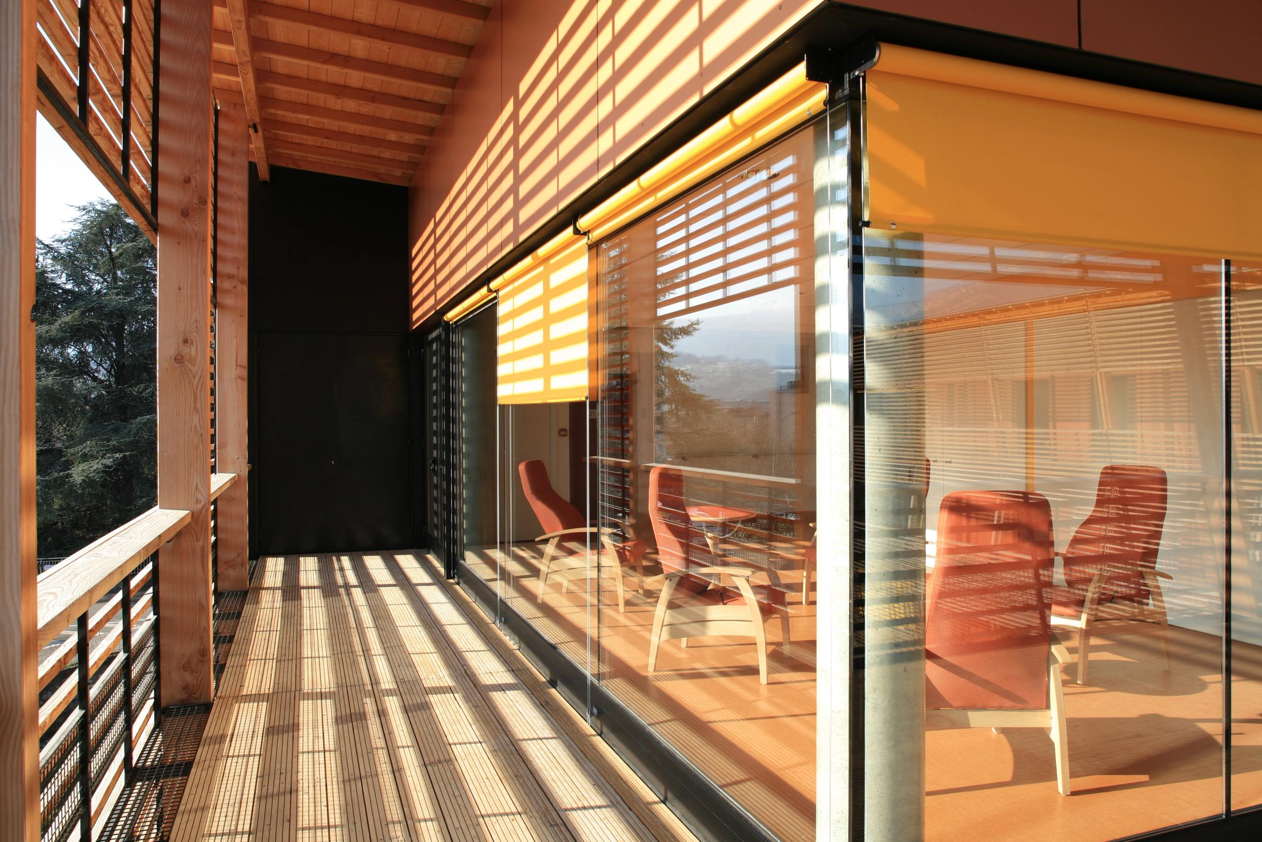 Terrasse bois de l’EHPAD de Chambéry par Tectoniques, protégée par brise-soleil et stores, ouvrant par de larges vitrages sur un salon résidentiel.