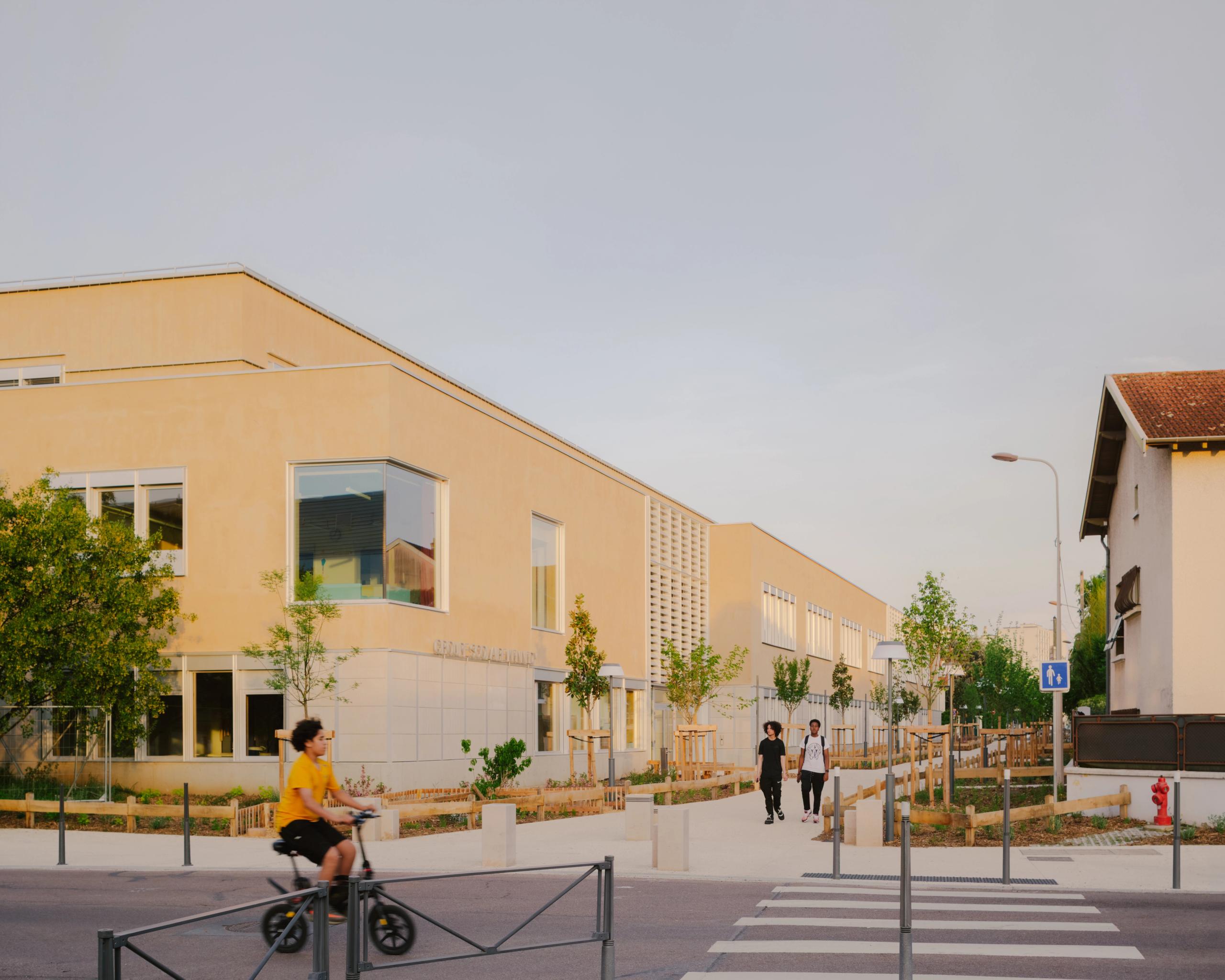 Vue de la façade minérale du groupe scolaire Kennedy à Lyon, volumes simples en équerre sur rue, grandes baies vitrées et cour plantée en premier plan.