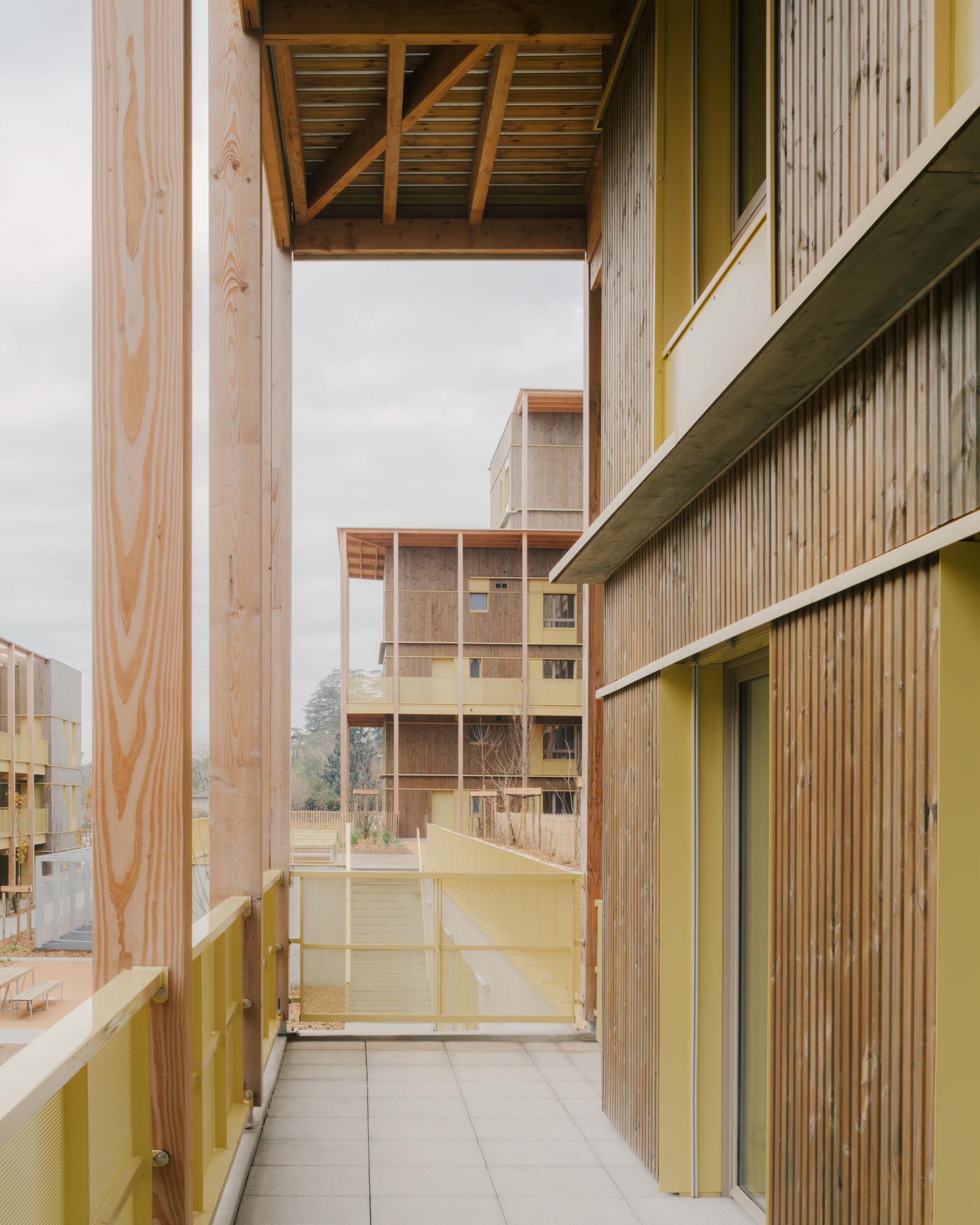 Livraison des 84 logements à Trévoux par Tectoniques : coursive en bois et serrurerie jaune cadrant des volumes en gradins, façades à ossature bois et balcons filants.