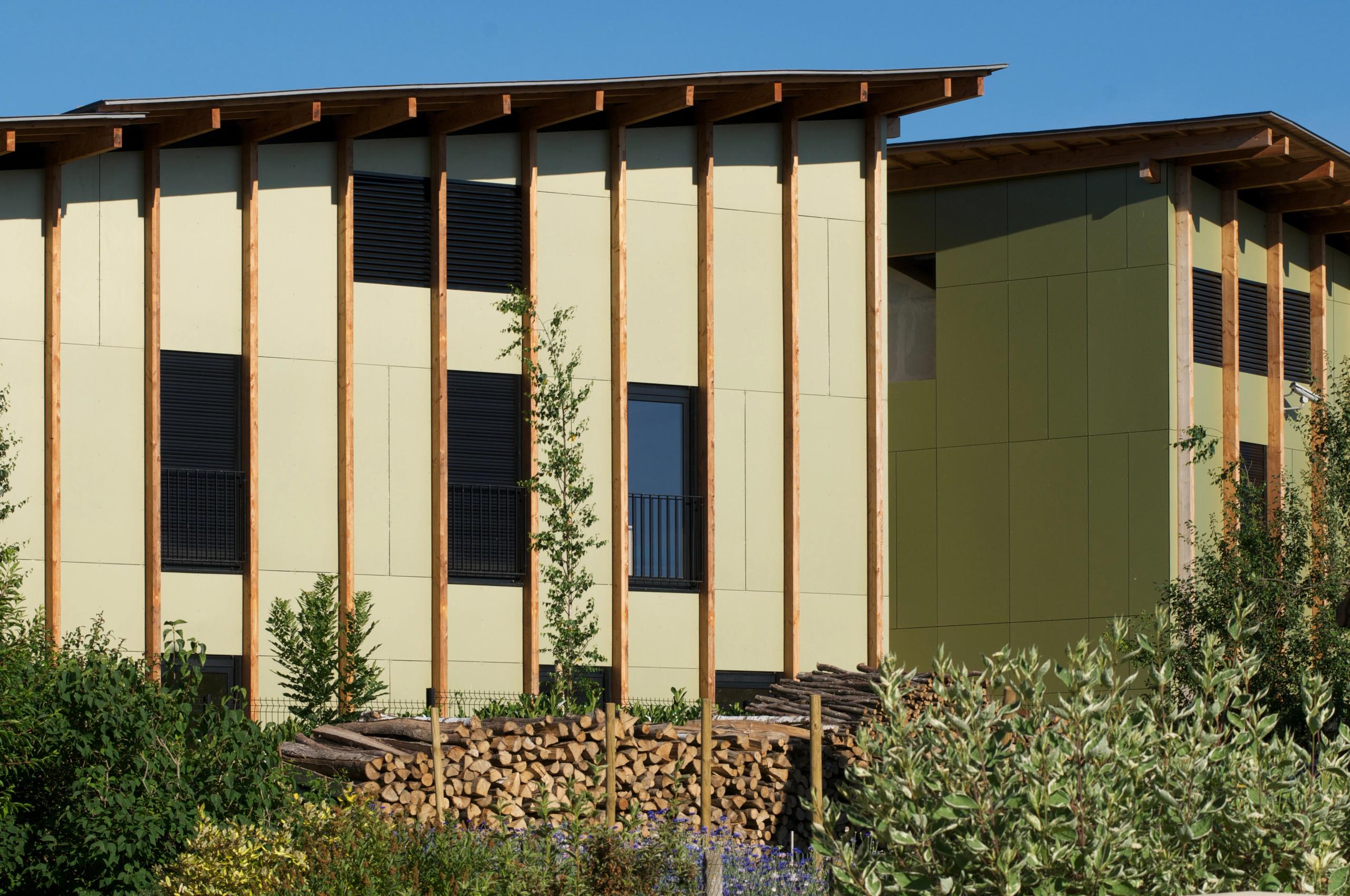 Façade de l’EHPAD de Mervans par Tectoniques, volumes bois et panneaux vert clair rythmés par poteaux verticaux, toiture débordante et jardin planté au premier plan.