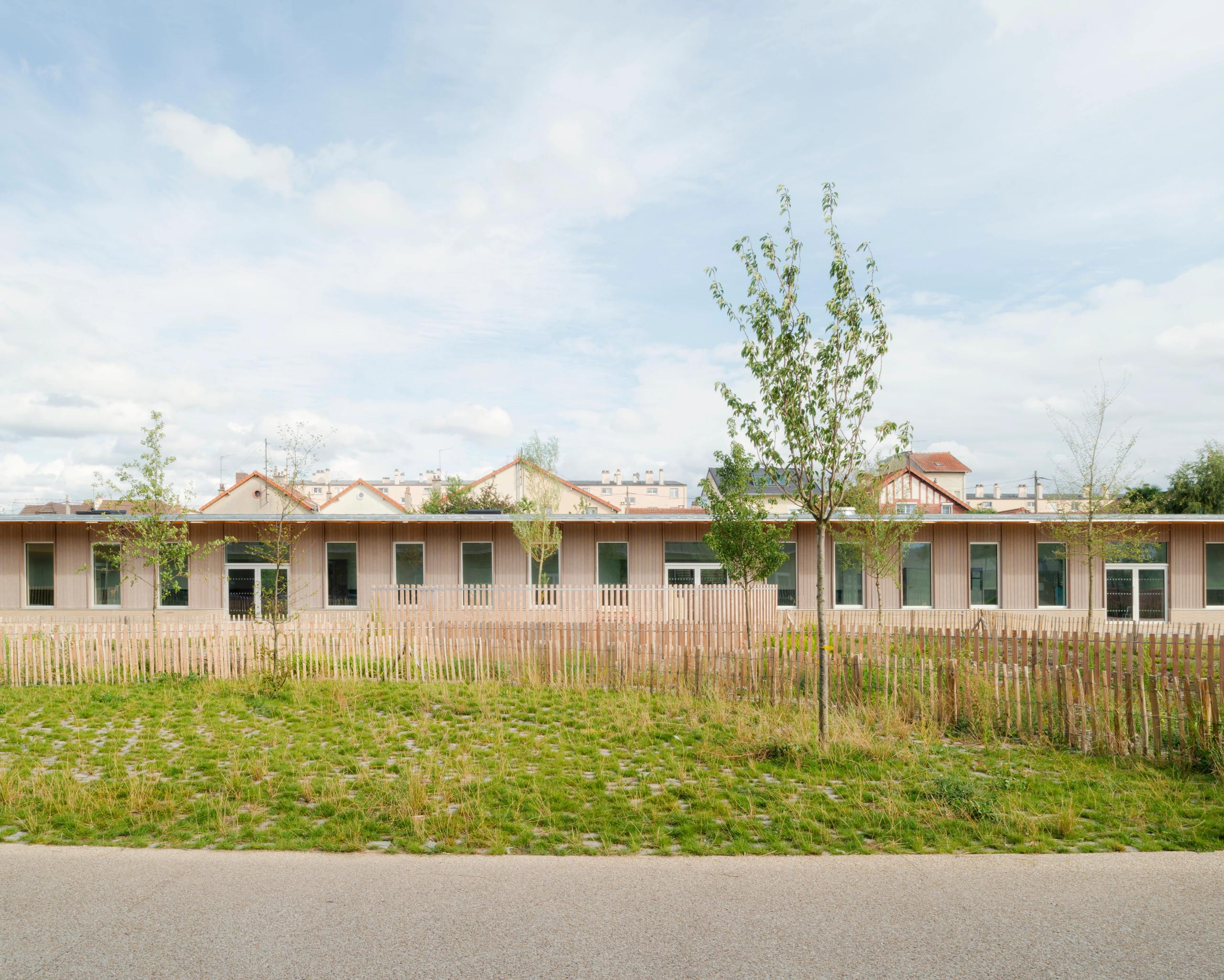 Façade sur parc des groupes scolaires Jacqueline Auriol et Jean Jaurès au Bourget, volume bas en U, bardage bois, grandes baies et clôture légère sur jardin.