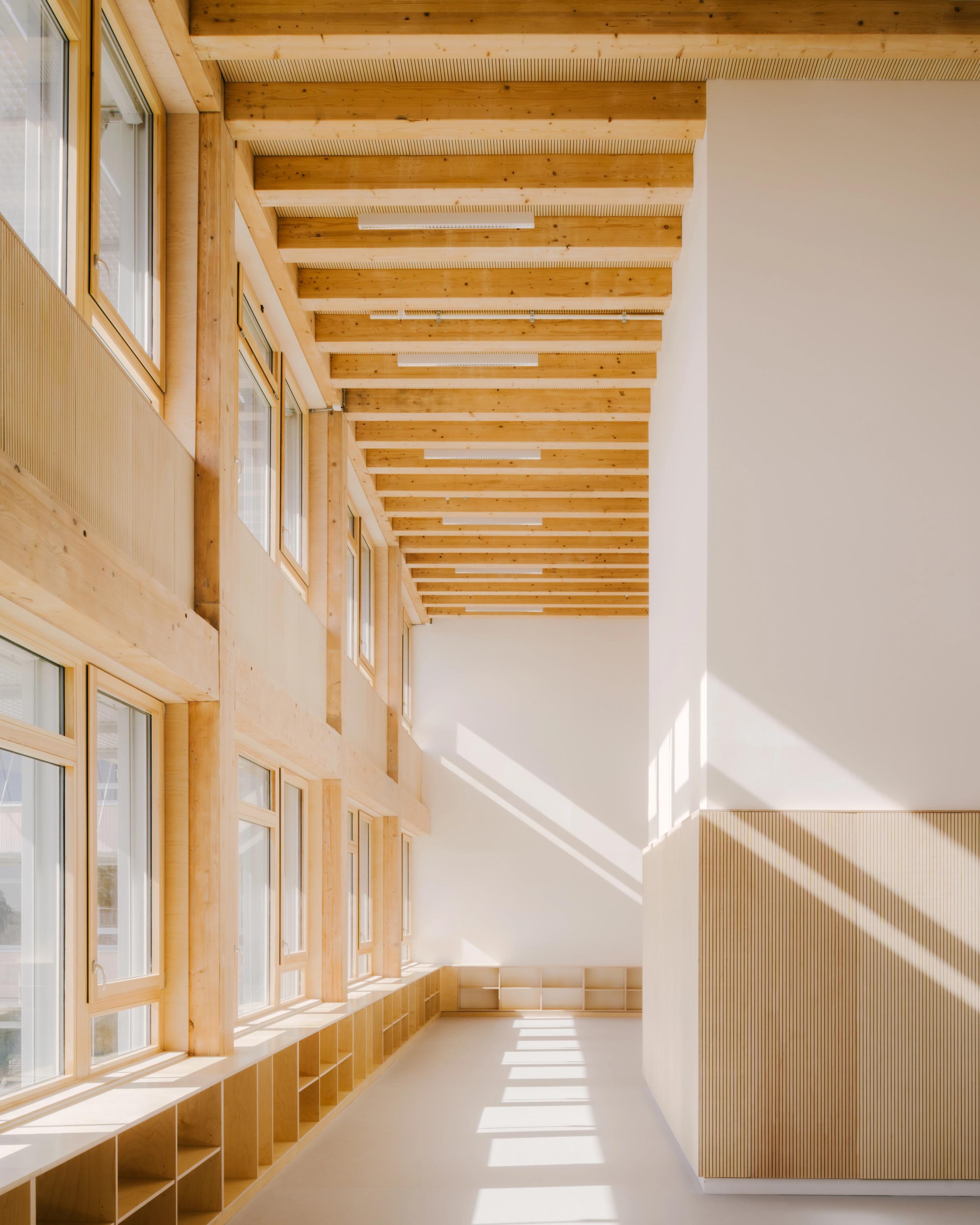 Galerie intérieure du Groupe scolaire Dominique Frelaut à Colombes, structure bois apparente, grandes baies vitrées et lumière naturelle traversante.