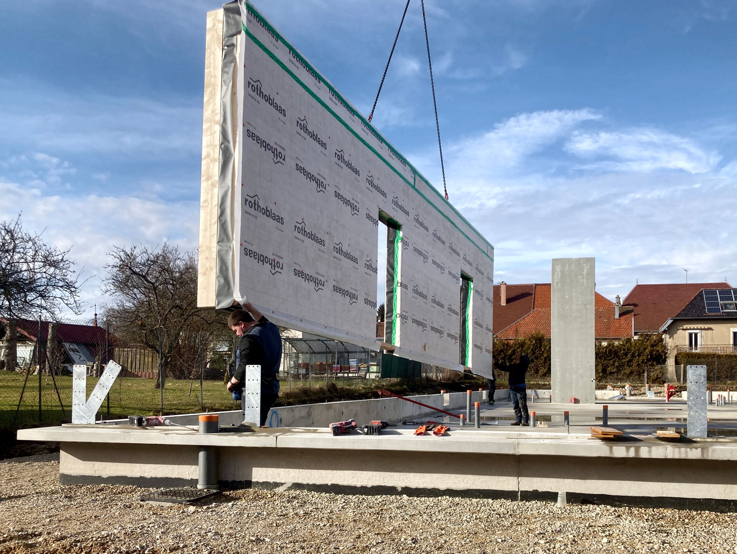 Montage d’un mur ossature bois préfabriqué du groupe scolaire Louis Pergaud à Levier, gruté sur la dalle béton, montrant la filière sèche et la structure du futur atrium.
