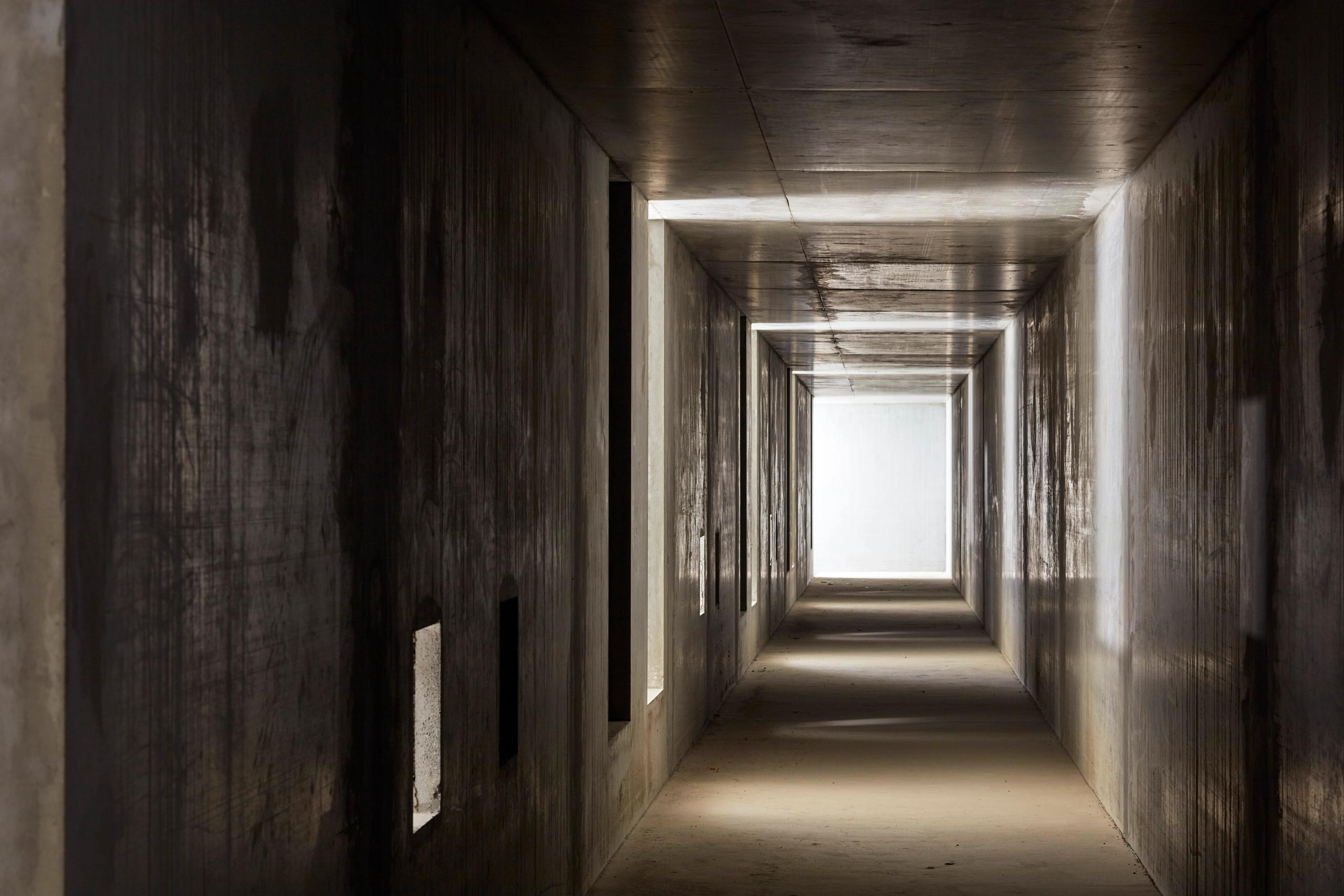 Couloir technique en béton brut du poste source de Cusset à Villeurbanne, en triple hauteur, éclairé par un jour terminal et des percements latéraux.