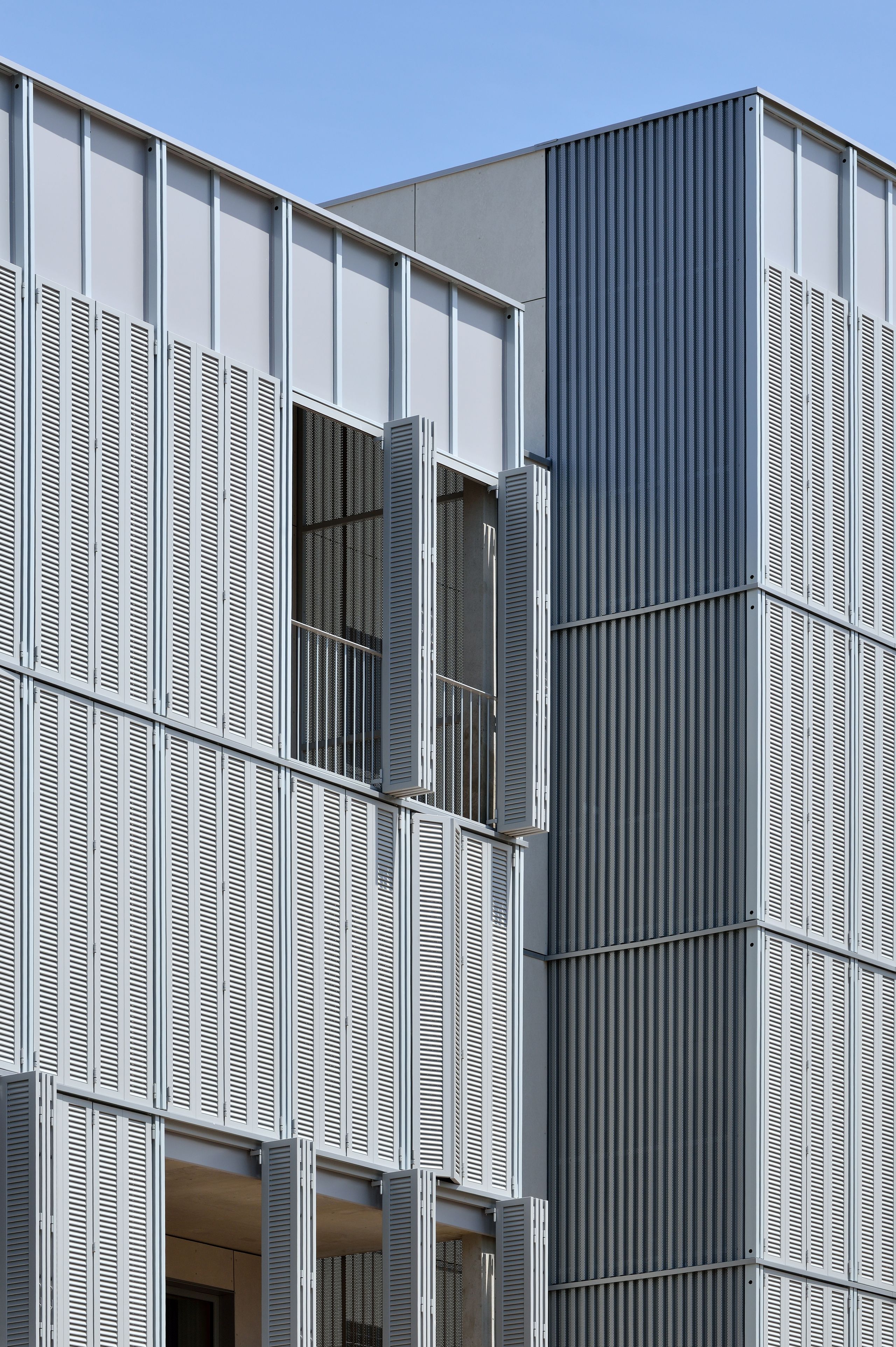 Façade des 28 logements à Villeurbanne par Tectoniques, en bardage métallique ajouré et nervuré, loggias protégées par persiennes coulissantes.