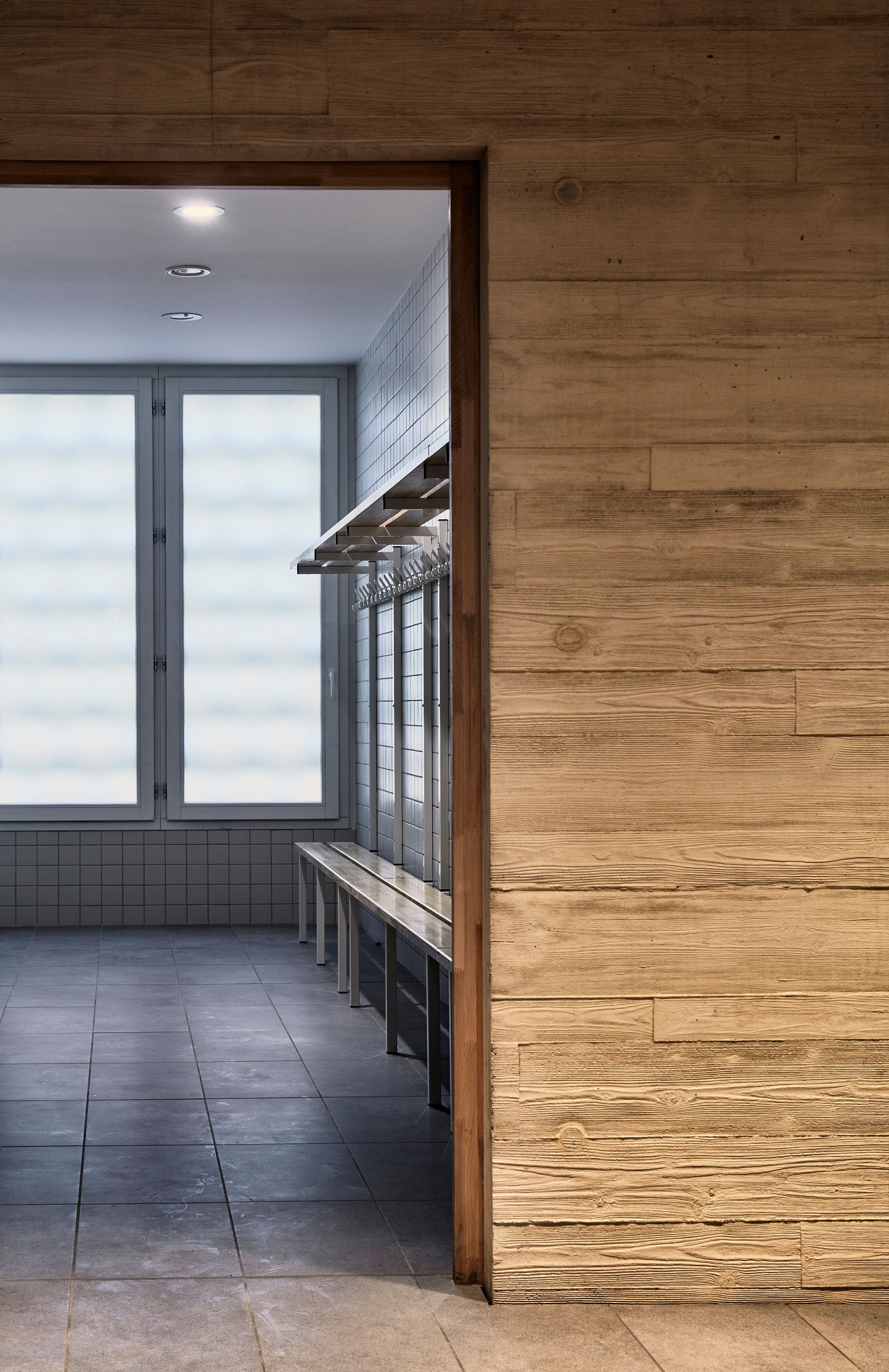 Maison des Arts à Charbonnières-les-Bains, vue intérieure d’un volume en béton et bois, vestiaire carrelé éclairé par une grande baie vitrée diffuse