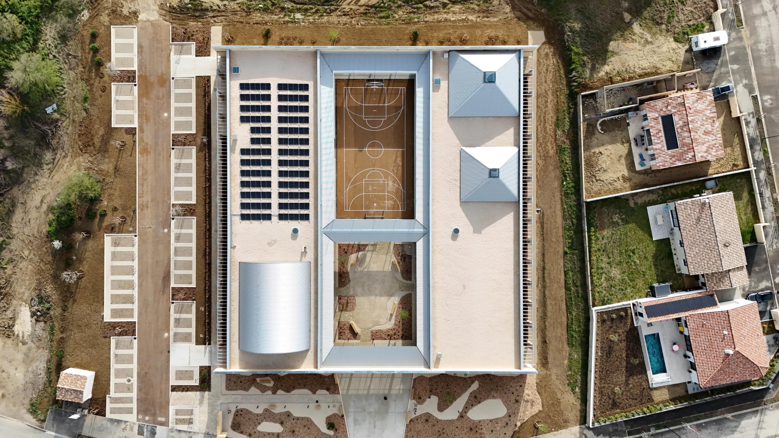 Aerial view of the Youth Cultural Center in Vaison-la-Romaine, a stone-framed courtyard complex with central sports court, garden and solar roofs.