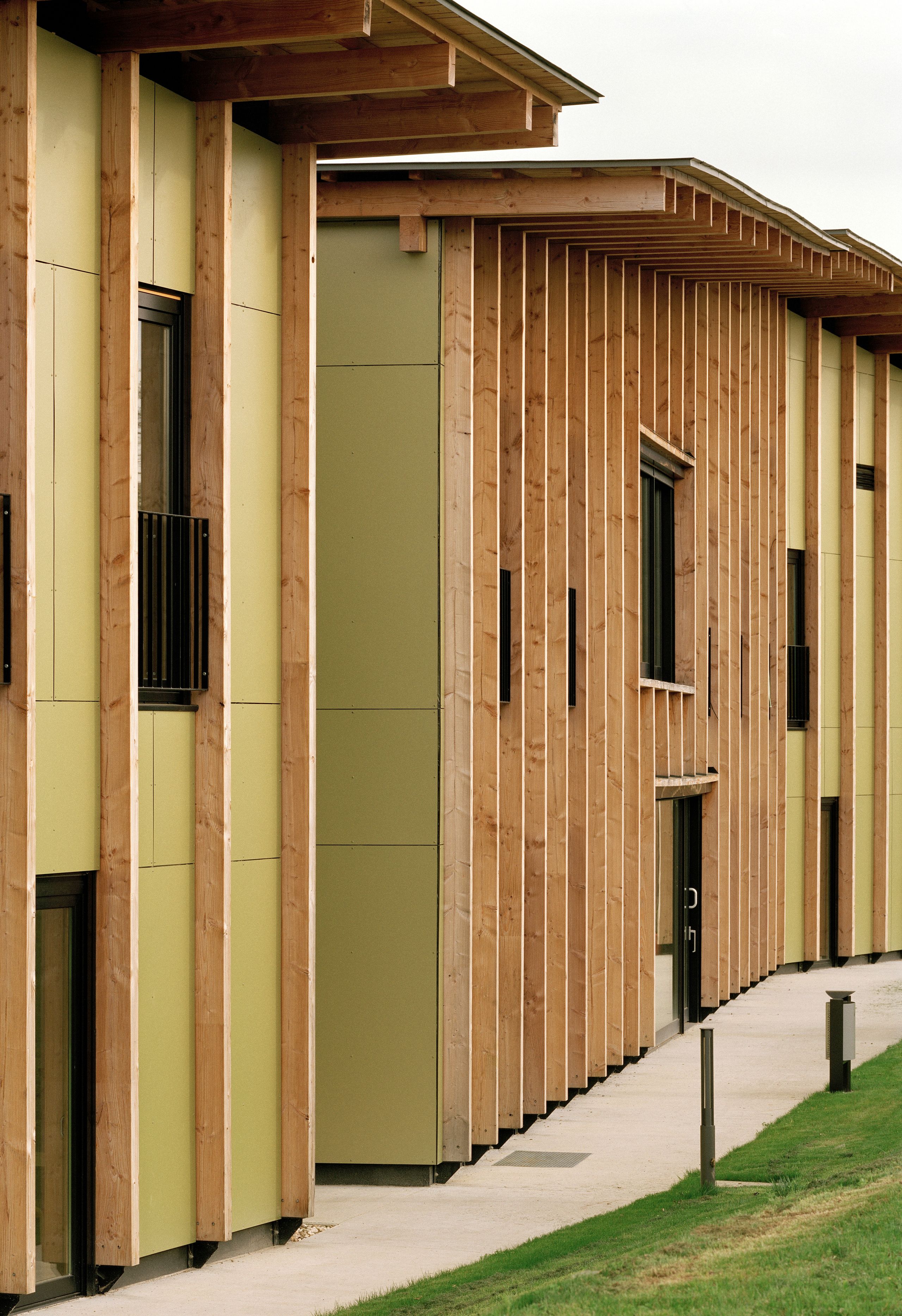 Façade de l’EHPAD de Mervans par Tectoniques : volumes linéaires en ossature bois, panneaux vert clair, toiture débordante rythmée, cheminement en pied de bâtiment.