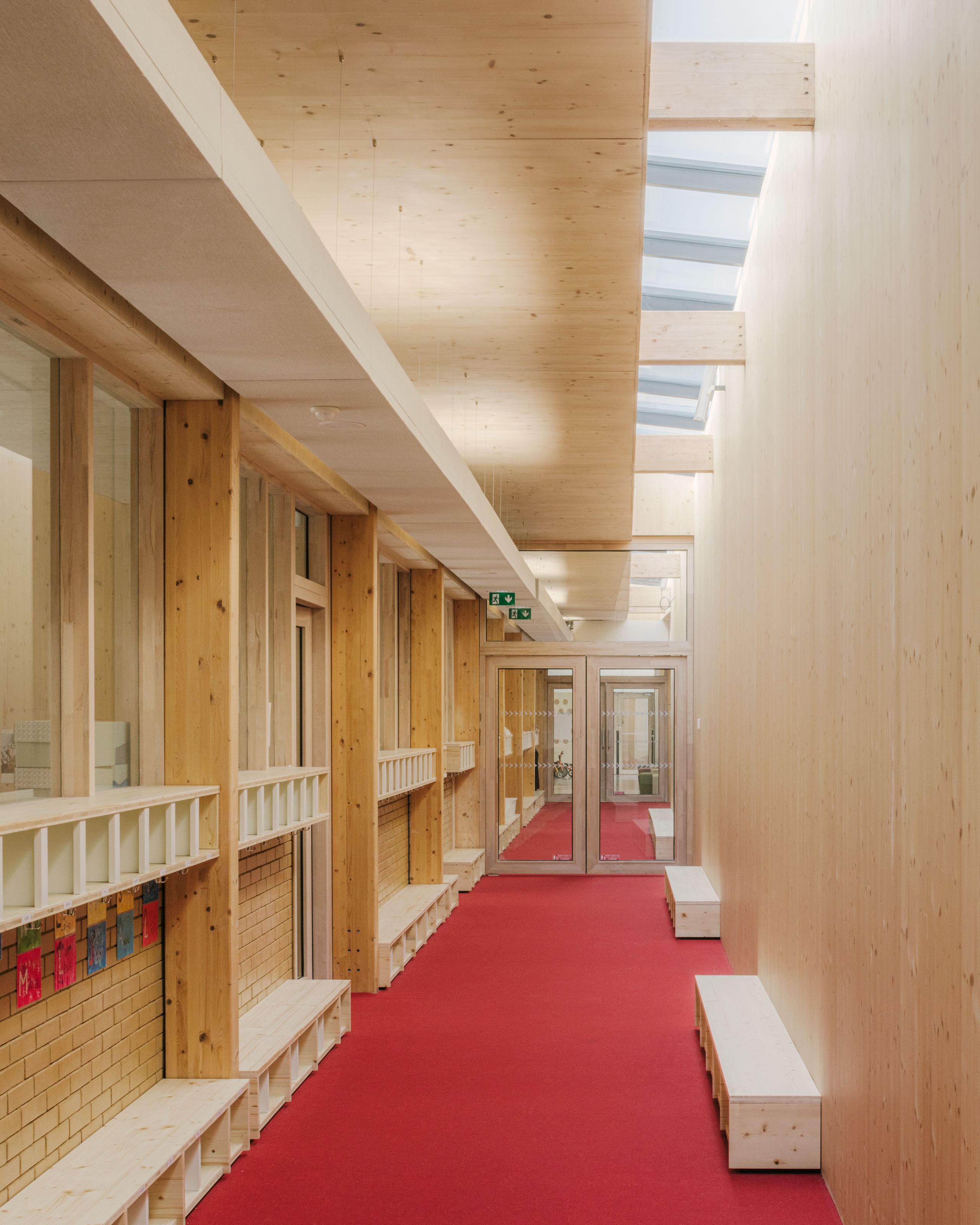 Couloir du groupe scolaire Claudie Haigneré aux Pennes-Mirabeau, structure bois apparente, lumière zénithale et sol rouge structurant la circulation.
