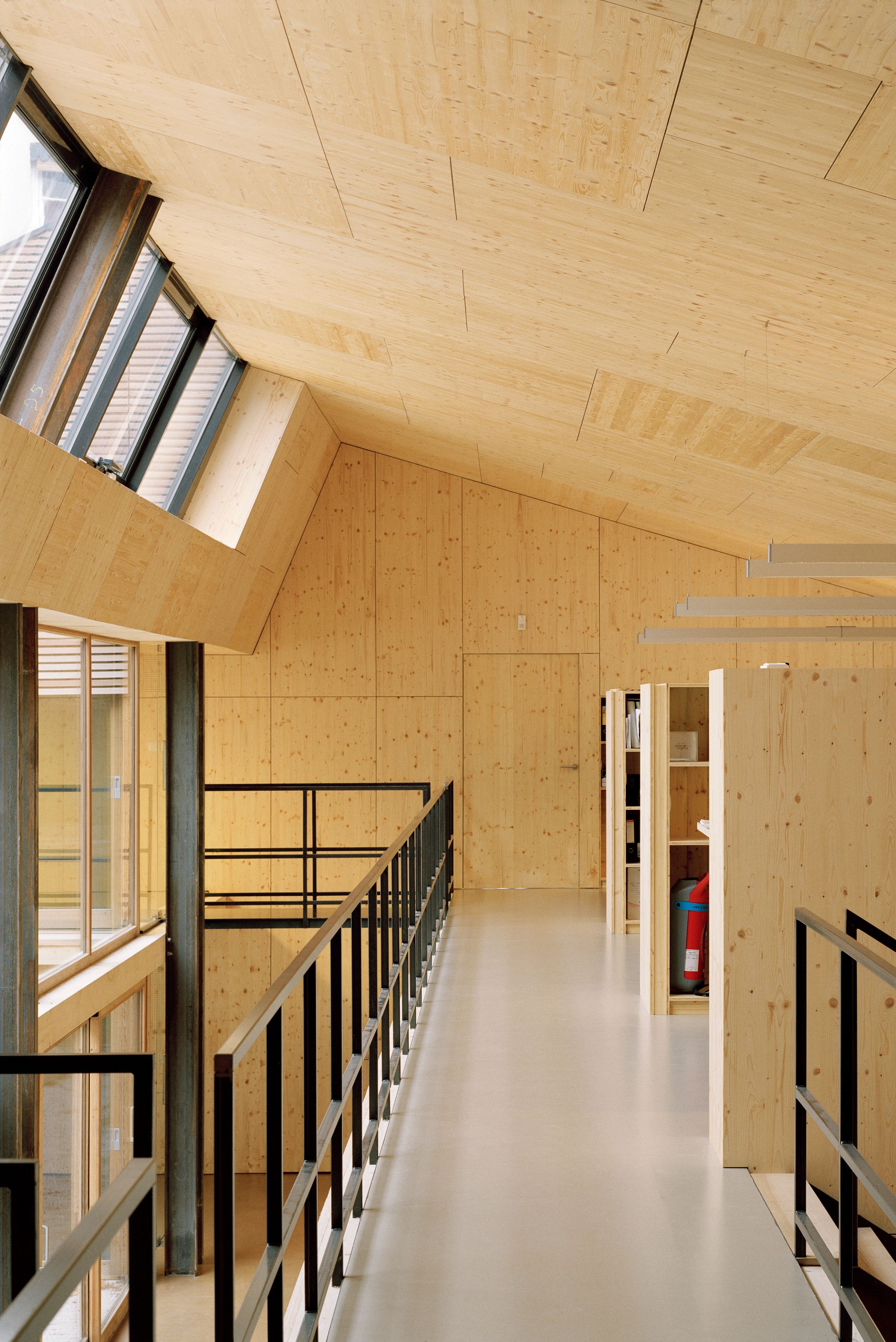Réhabilitation d’un local d’activité à Lyon par Tectoniques : mezzanine en bois lamellé, garde-corps métalliques et lumière zénithale sur patio intérieur.