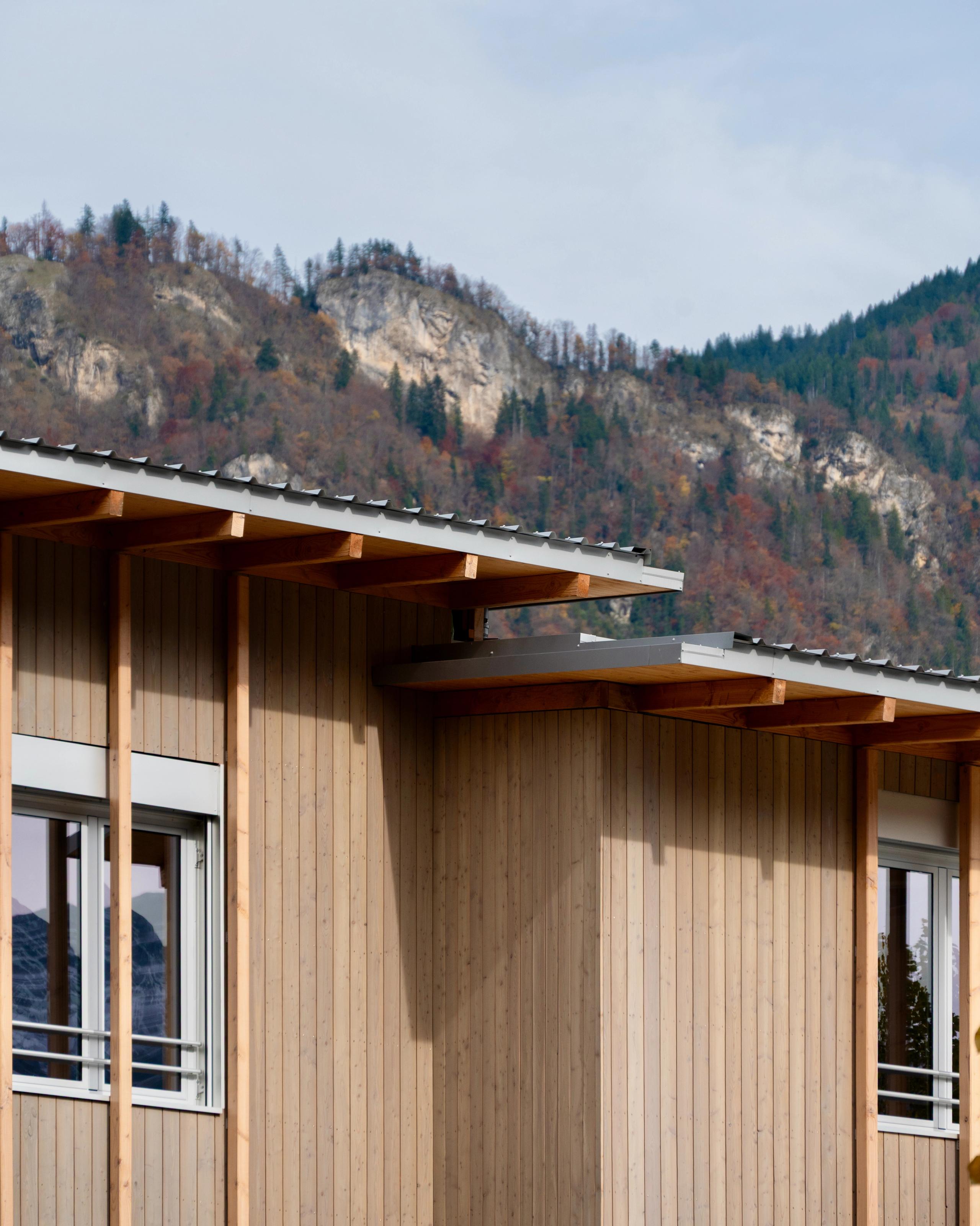 Façade en ossature bois surélevée du groupe scolaire du Bouchet à Bonneville, bardage vertical clair, toitures débordantes en métal, paysage montagneux en arrière-plan.