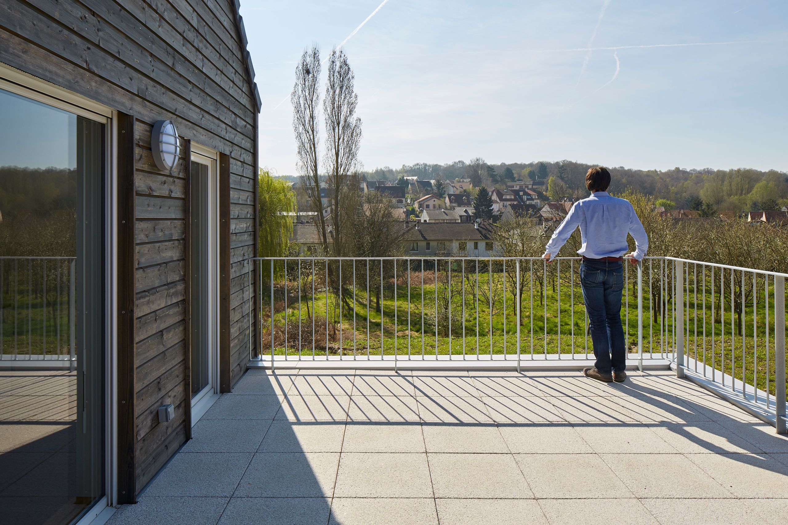 Terrasse des 36 logements Tectoniques à Vauhallan, dallage clair, garde-corps métallique fin et façade en bardage bois ouvrant sur le paysage vallonné.