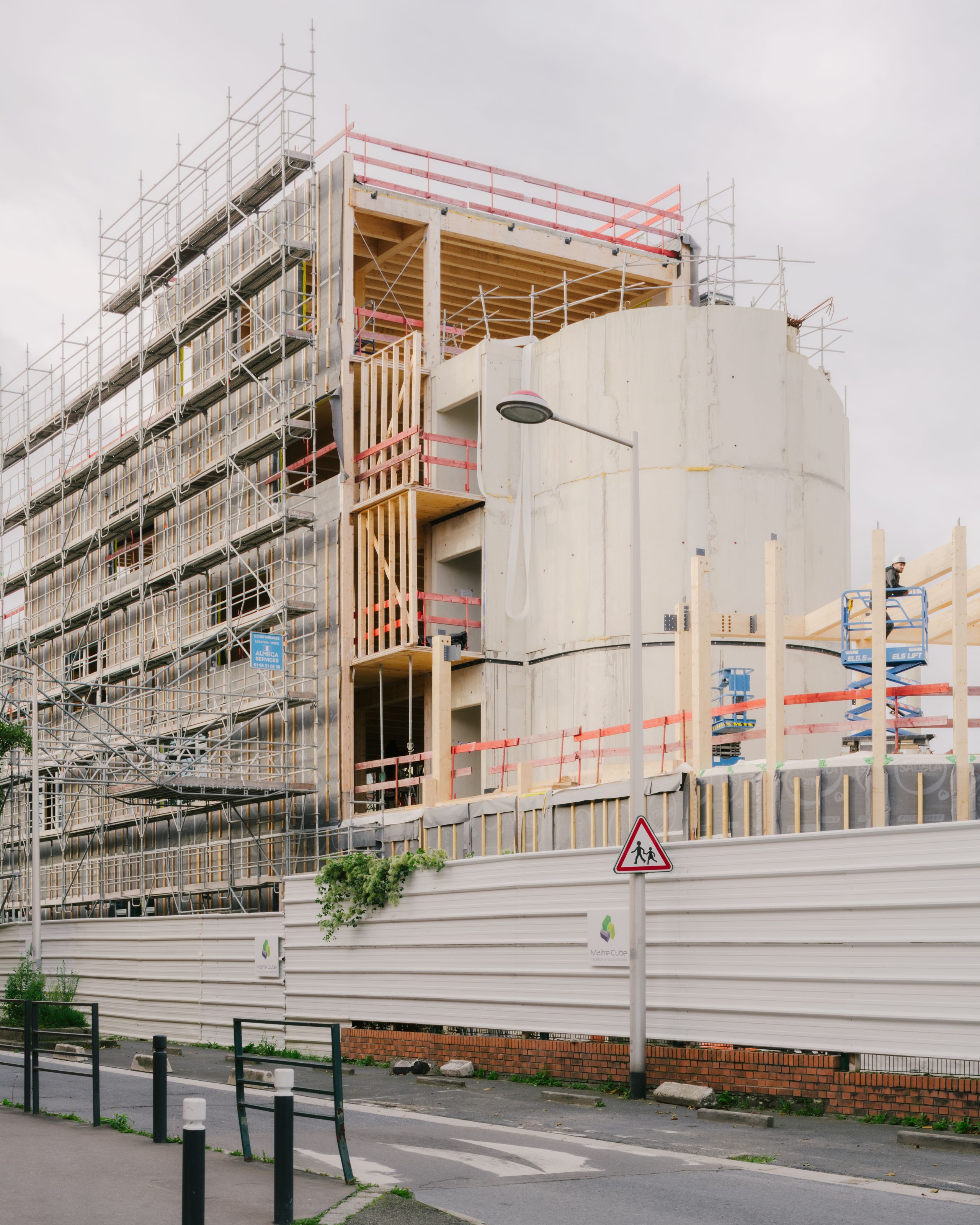 Chantier du groupe scolaire Dominique Frelaut à Colombes : volume courbe en béton, structure bois apparente et échafaudages le long de la rue urbaine.
