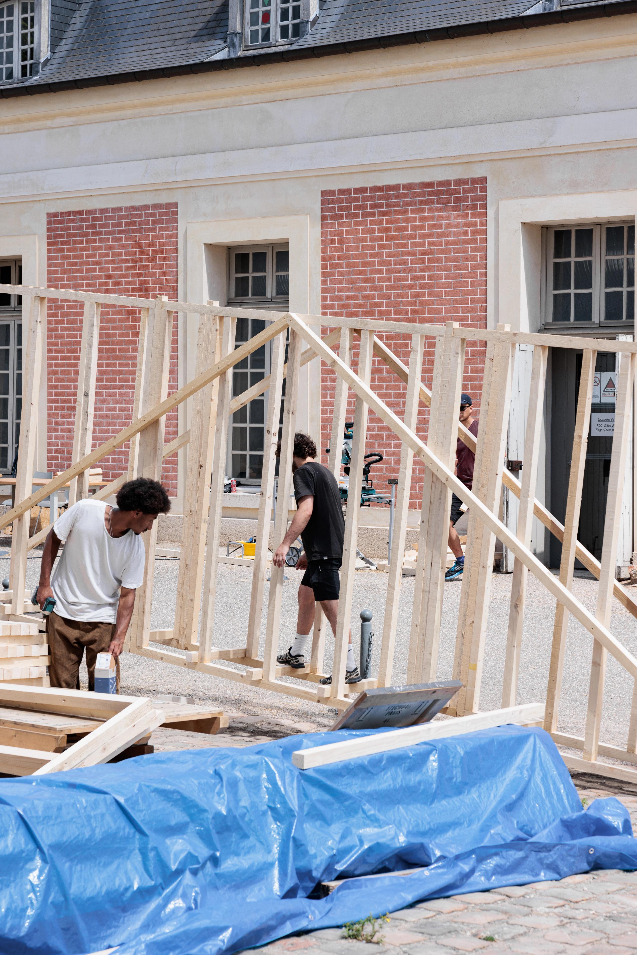 Montage in situ de la structure bois 60x60 du workshop Tectoniques à Versailles, ossature légère manuportable devant les façades en briques de l’école.