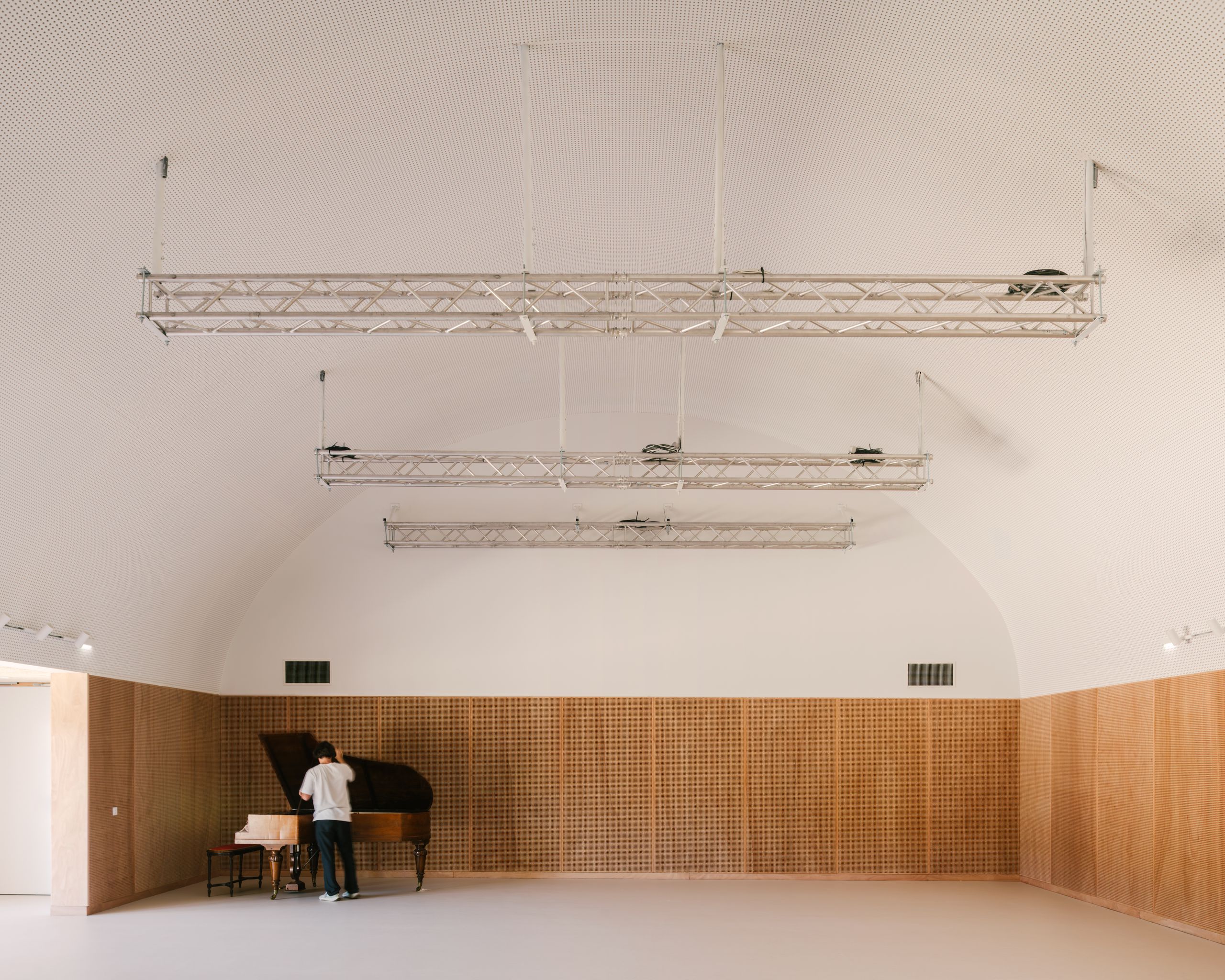Interior of the Youth Cultural Centre in Vaison-la-Romaine, showing a timber-lined performance hall with vaulted acoustic ceiling and suspended lighting grids.