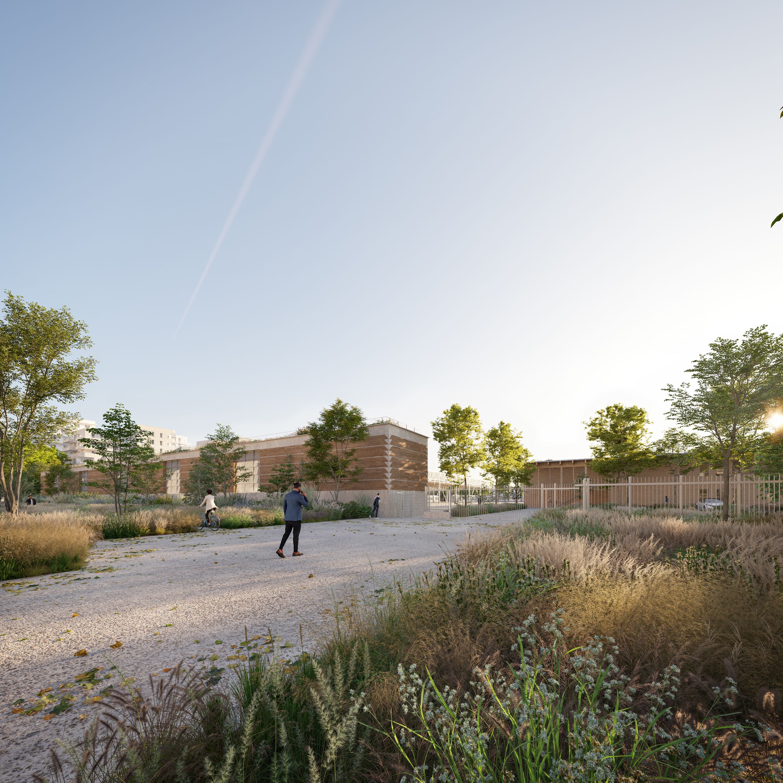 View of the Lyon tramway maintenance center with rammed-earth volumes, metal fencing and a landscaped forecourt with trees, grasses and pedestrian paths.